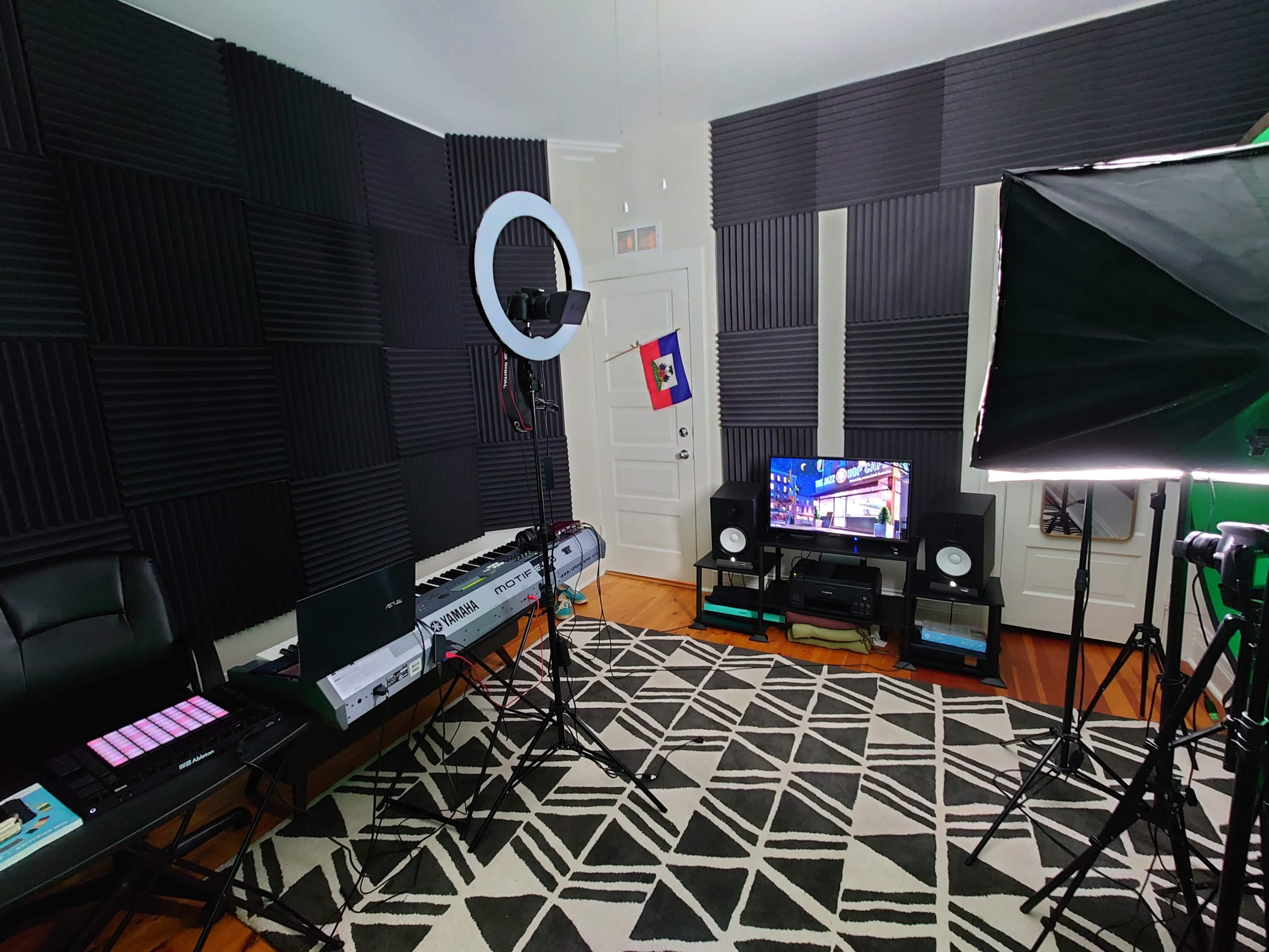 A recording studio setup with soundproof foam panels on the walls, a keyboard, a ring light, and a television on a black media console.