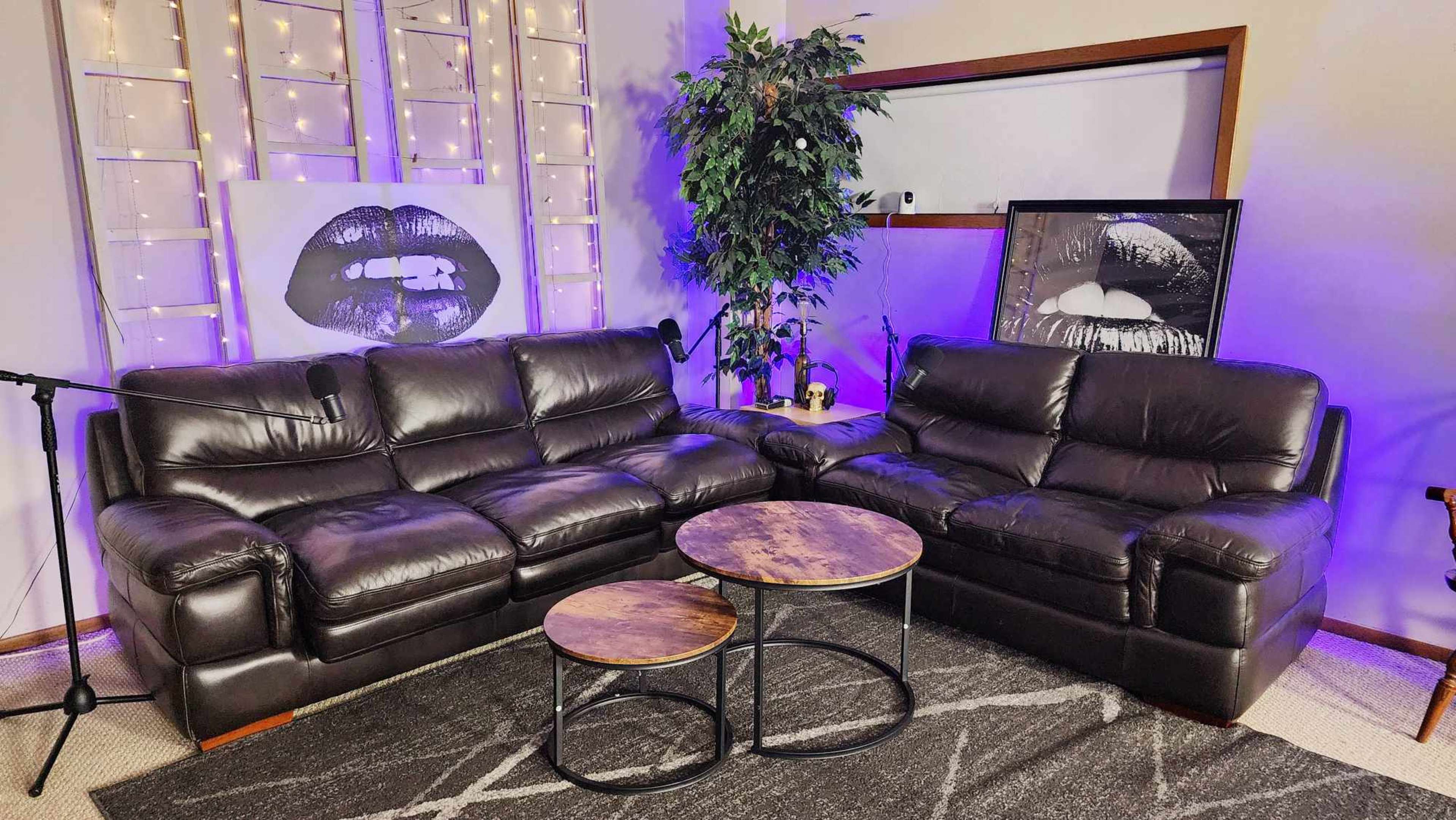 A cozy seating area with two dark leather sofas, a round wooden coffee table, and decor featuring large black and white lip illustrations against a softly lit backdrop.