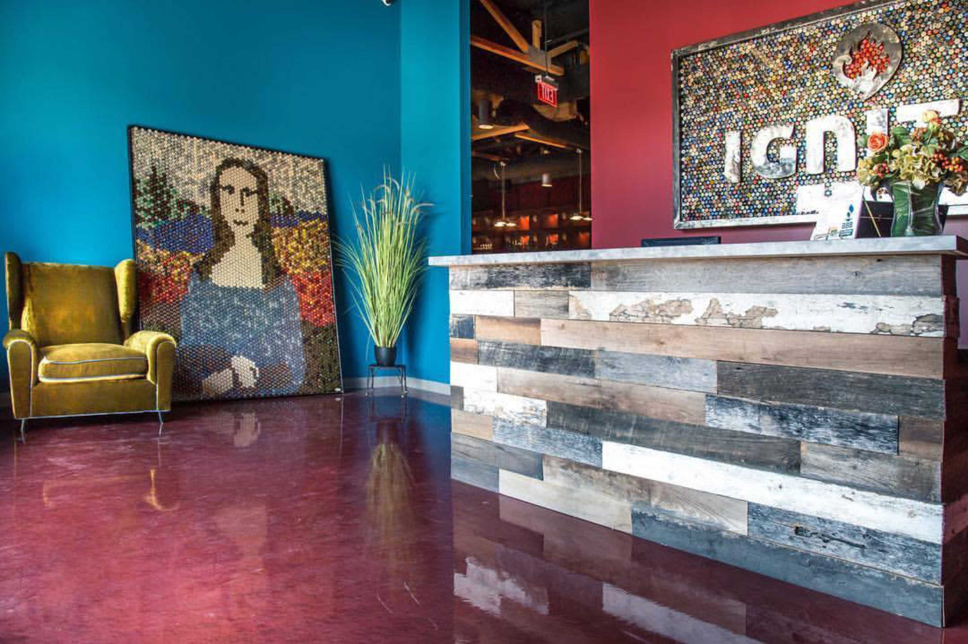 A brightly colored reception area featuring a wooden reception desk, a green armchair, and a mosaic artwork on the wall.