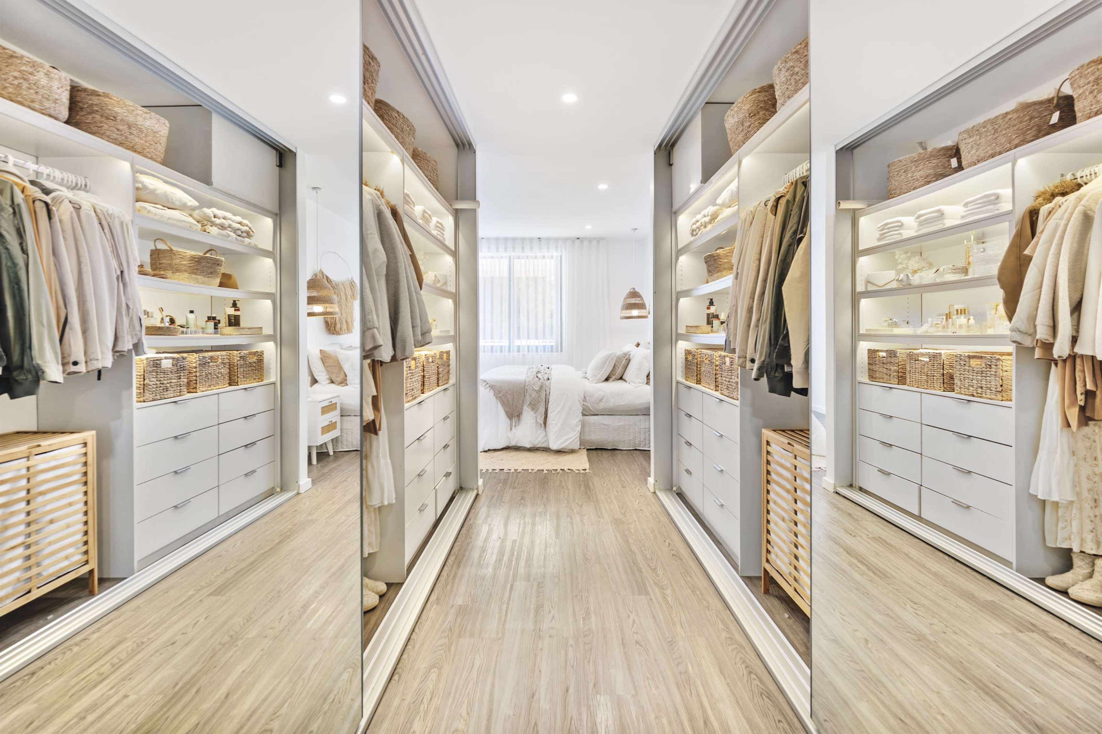 A well-organized walk-in closet featuring shelves, drawers, and clothing on display, leading into a bright bedroom with a bed and decorative items.