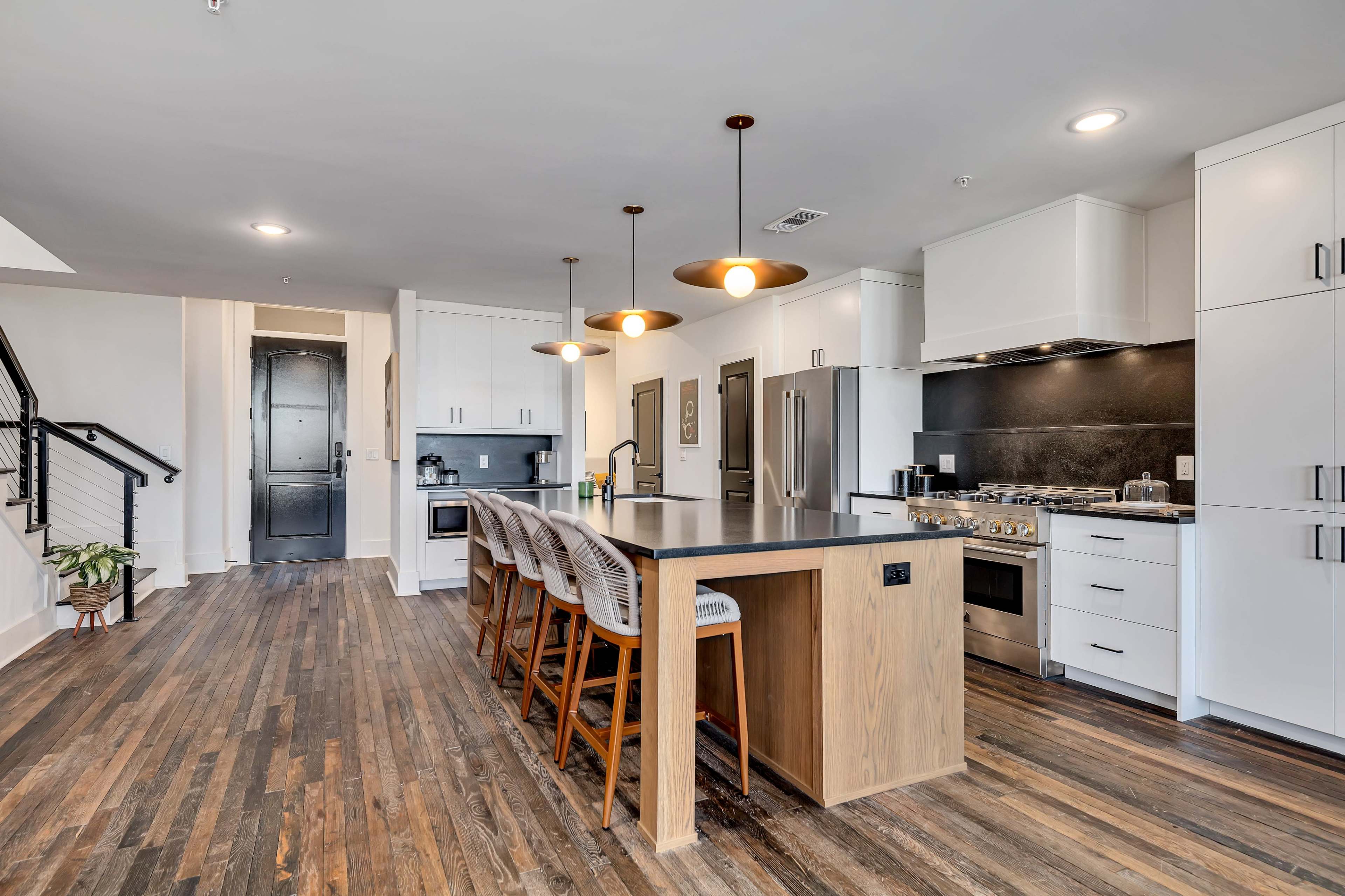 A modern kitchen featuring a large island with bar stools, stainless steel appliances, and white cabinets against a dark countertop.