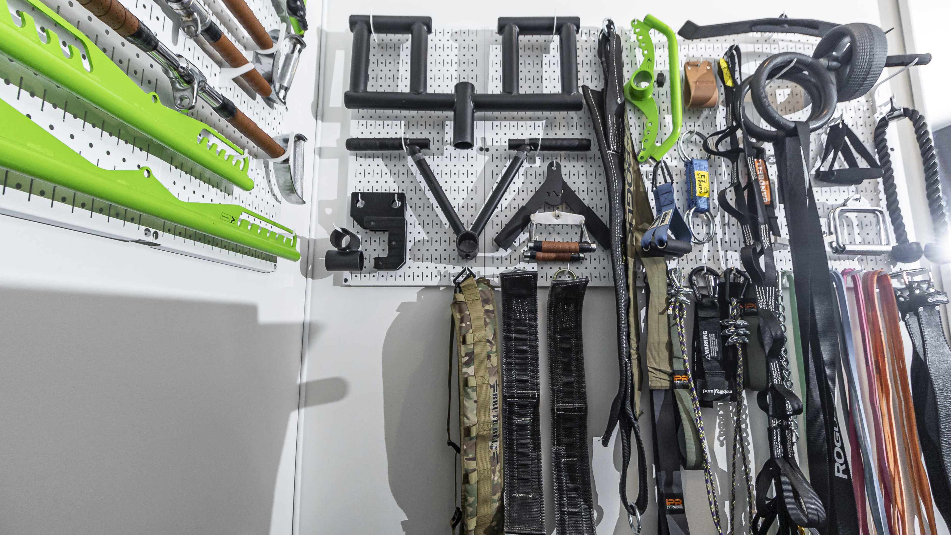 A pegboard mounted on a wall, displaying various tools and equipment, including green handles, straps, and a camouflage-patterned bag.
