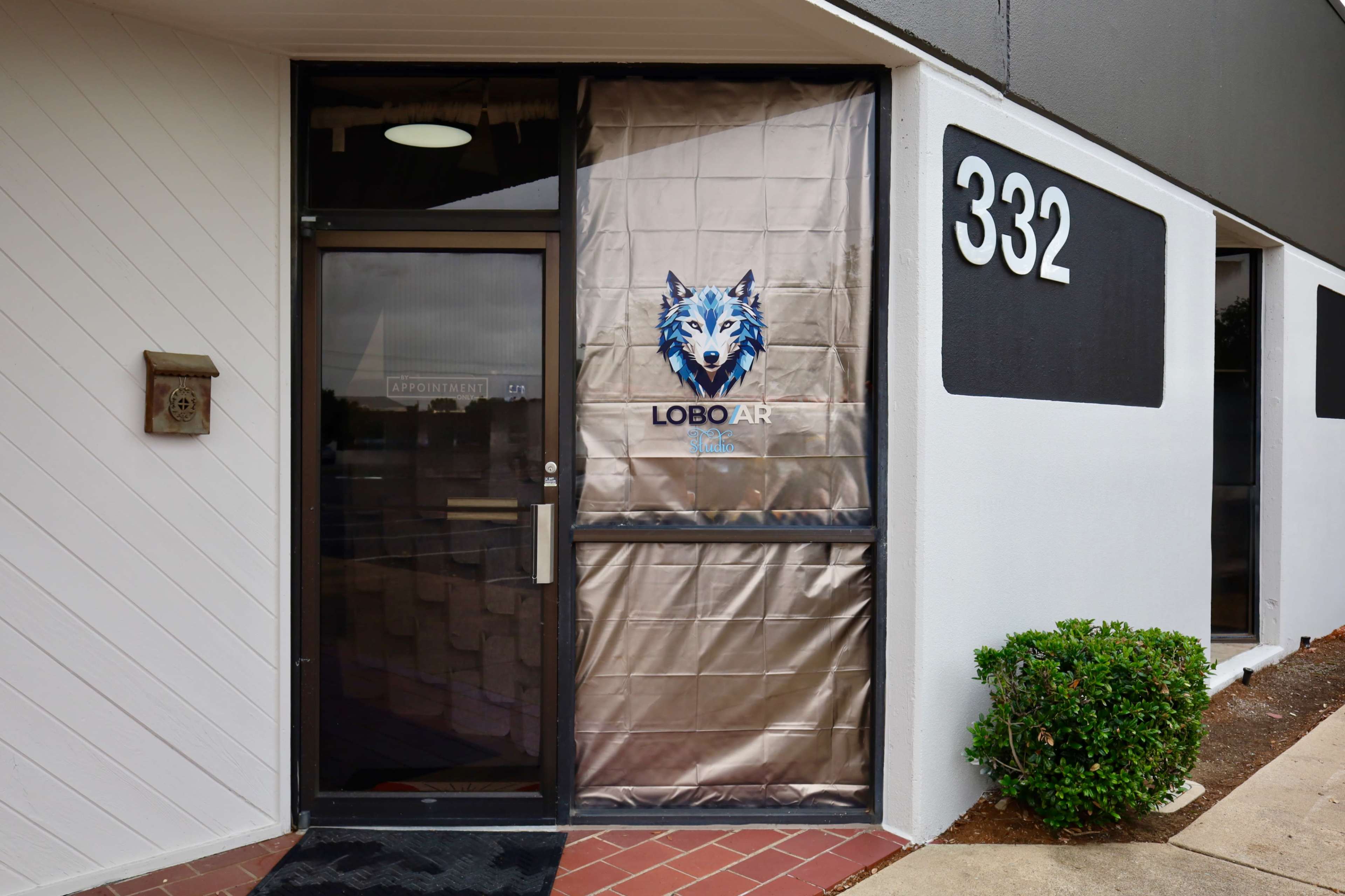 The image shows the entrance of a building with a door displaying a logo featuring a wolf and the text "LOBO AR," alongside the address number 332.