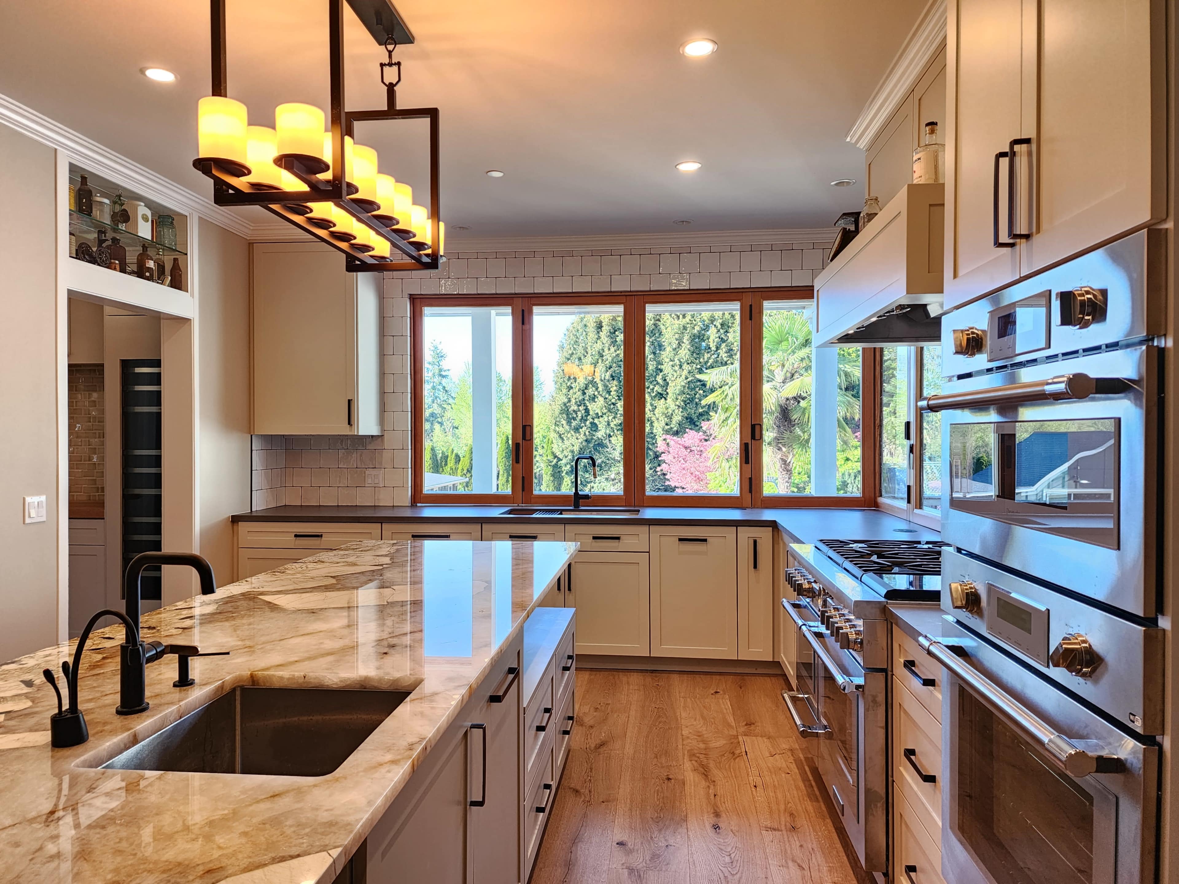 A modern kitchen features white cabinetry, stainless steel appliances, and a large island with a marble countertop, overlooking a view through multiple windows.