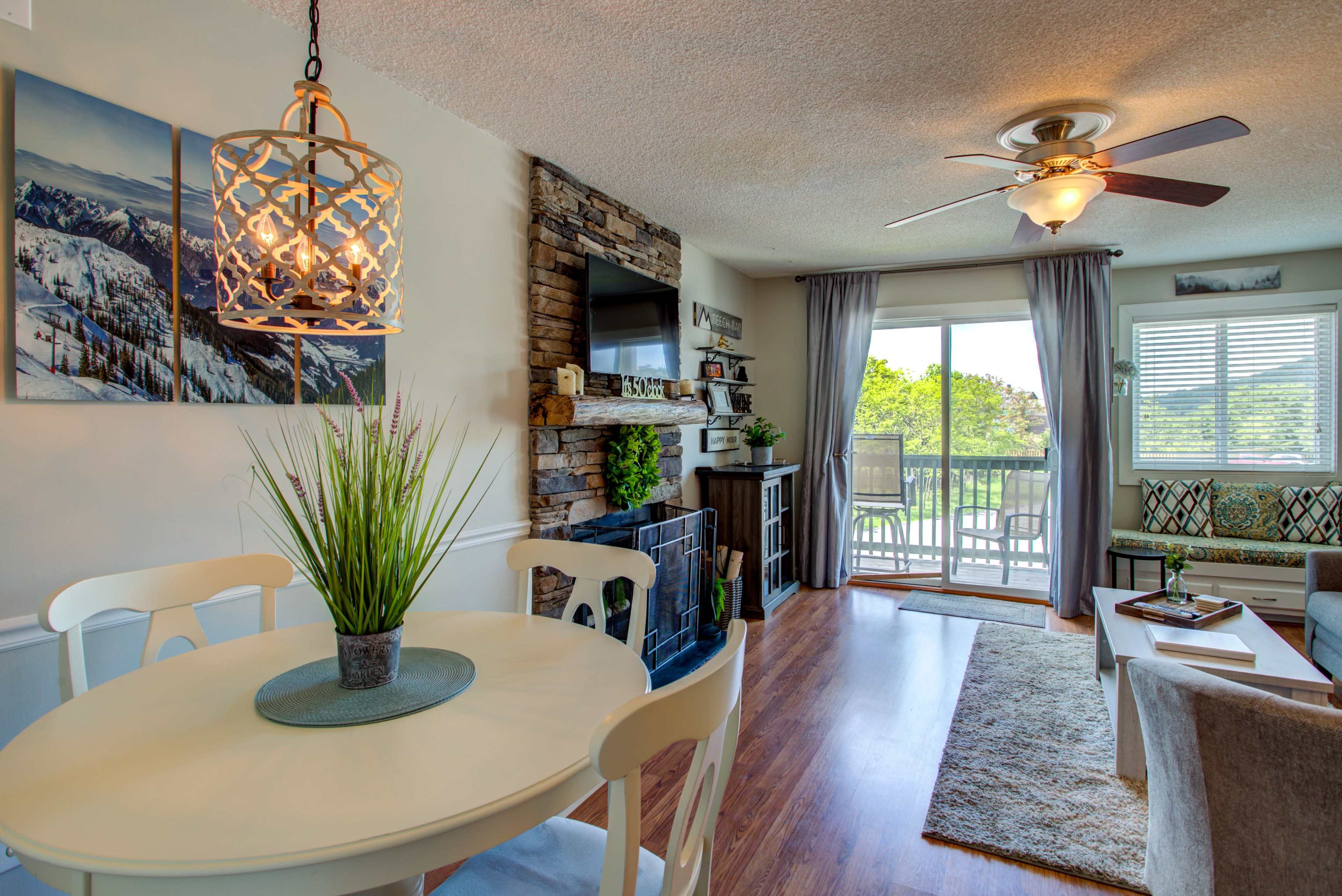 A dining area with a round table, a ceiling fan, and a view of a balcony is decorated with stone accents and a hanging light fixture.