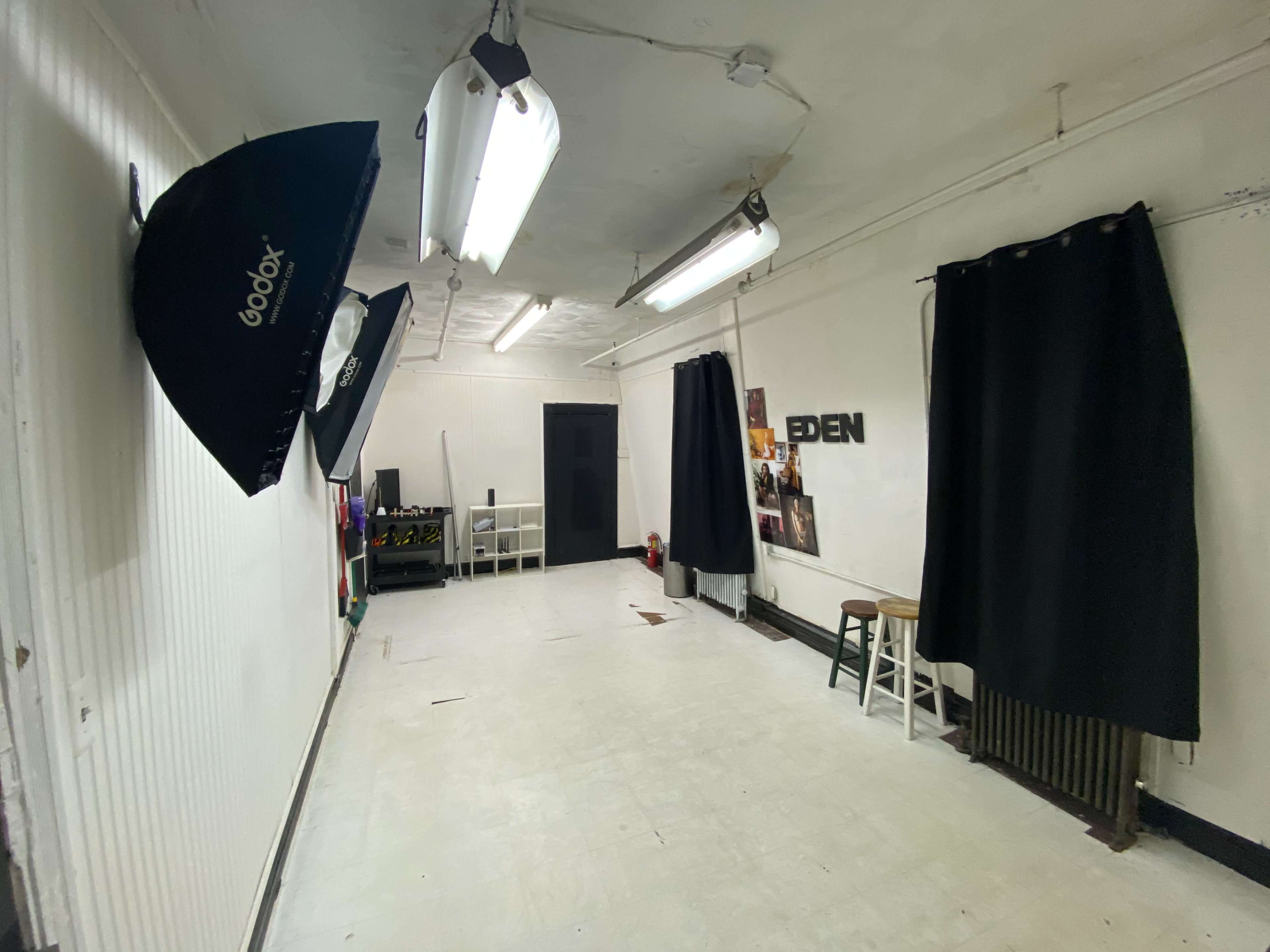 A narrow, empty room with fluorescent lights, a black curtain, photography equipment, and a door at one end.