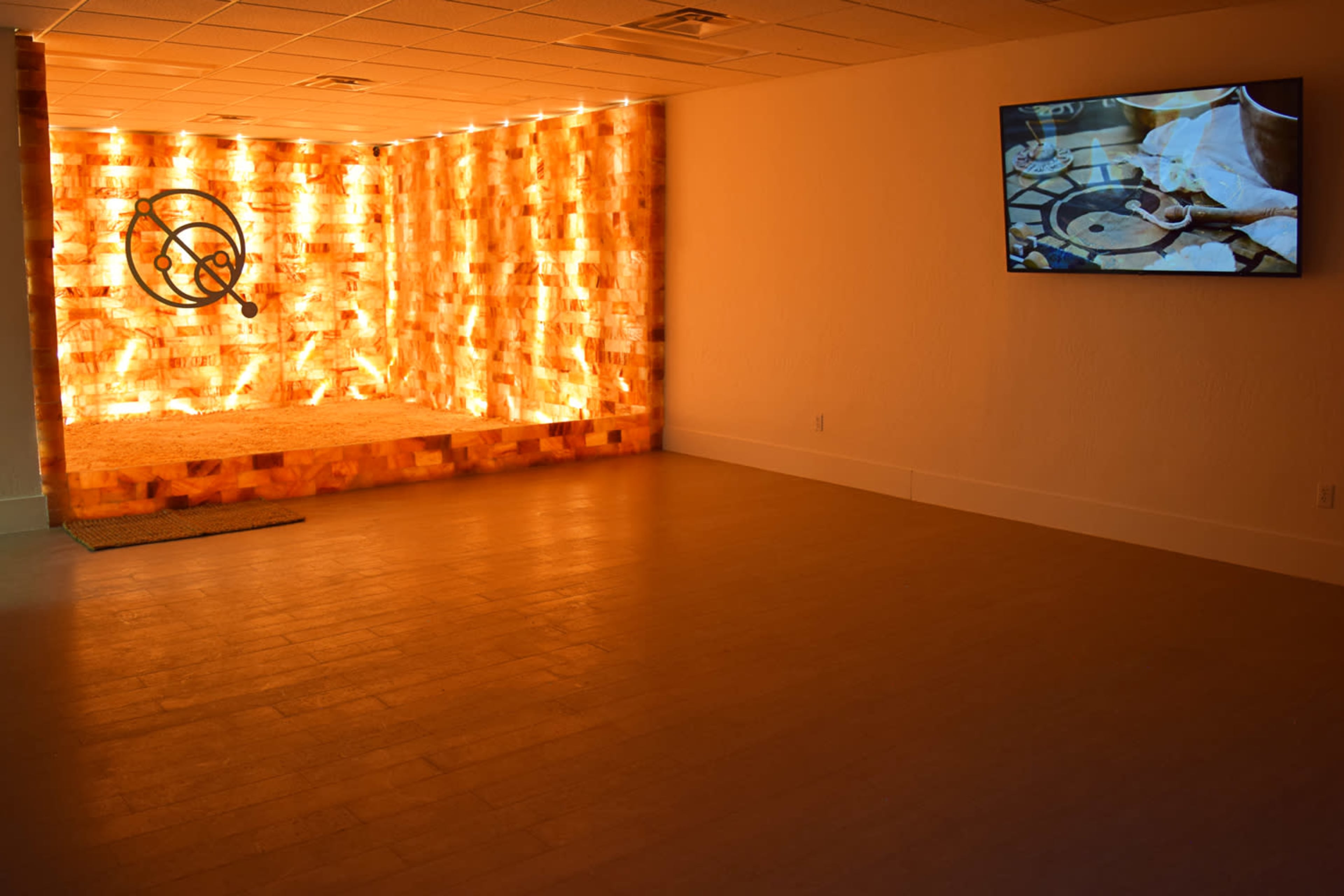 A well-lit room with a wall made of illuminated salt bricks and a television displaying a close-up of cooking ingredients.