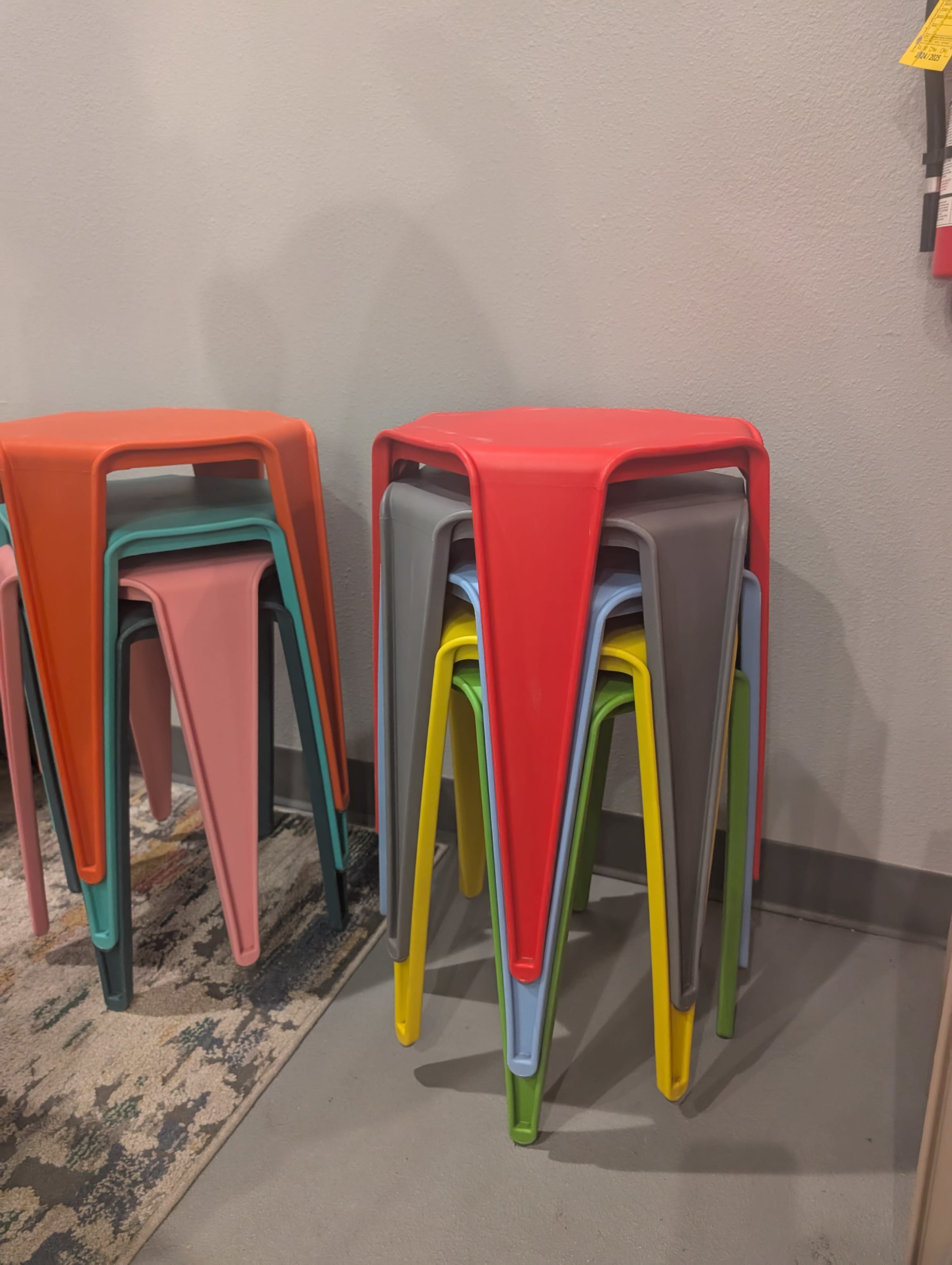 A stack of brightly colored plastic stools is positioned against a gray wall.