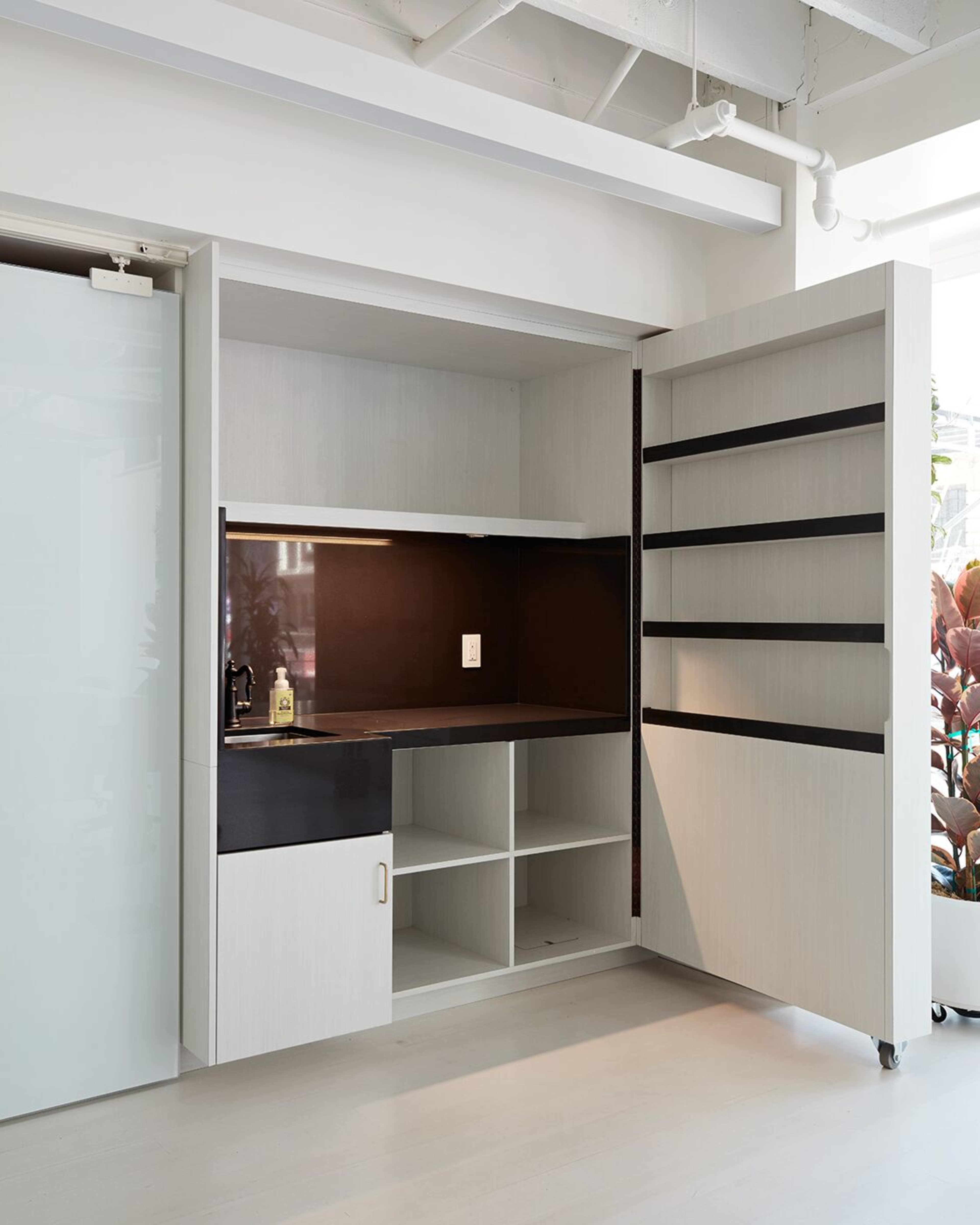 A compact kitchen area with a black countertop, shelving units, and closed storage cabinets on either side.