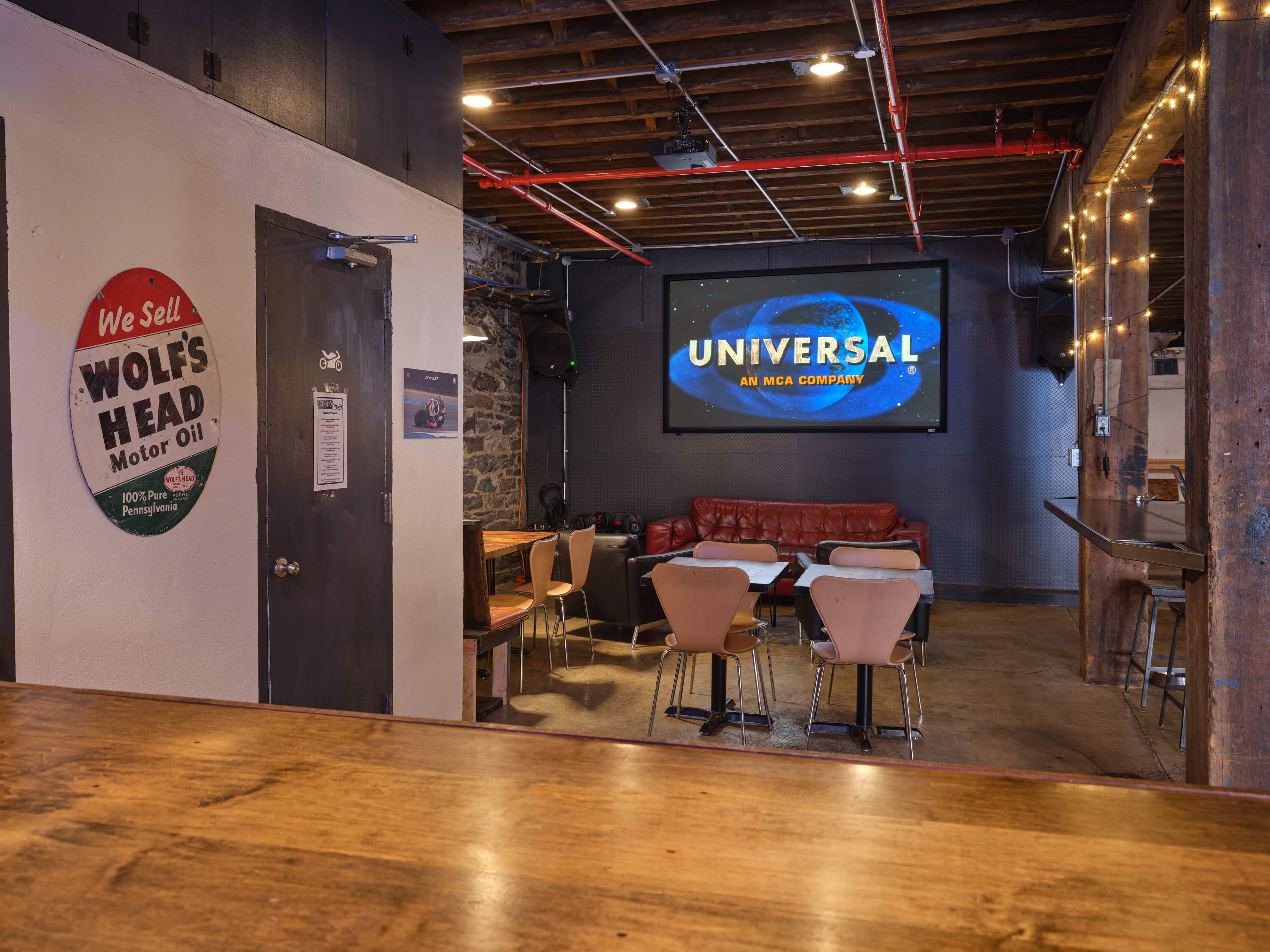 A dimly lit bar area features a large screen displaying "UNIVERSAL" on one wall, with seating arranged around tables and a leather couch along the opposite wall.