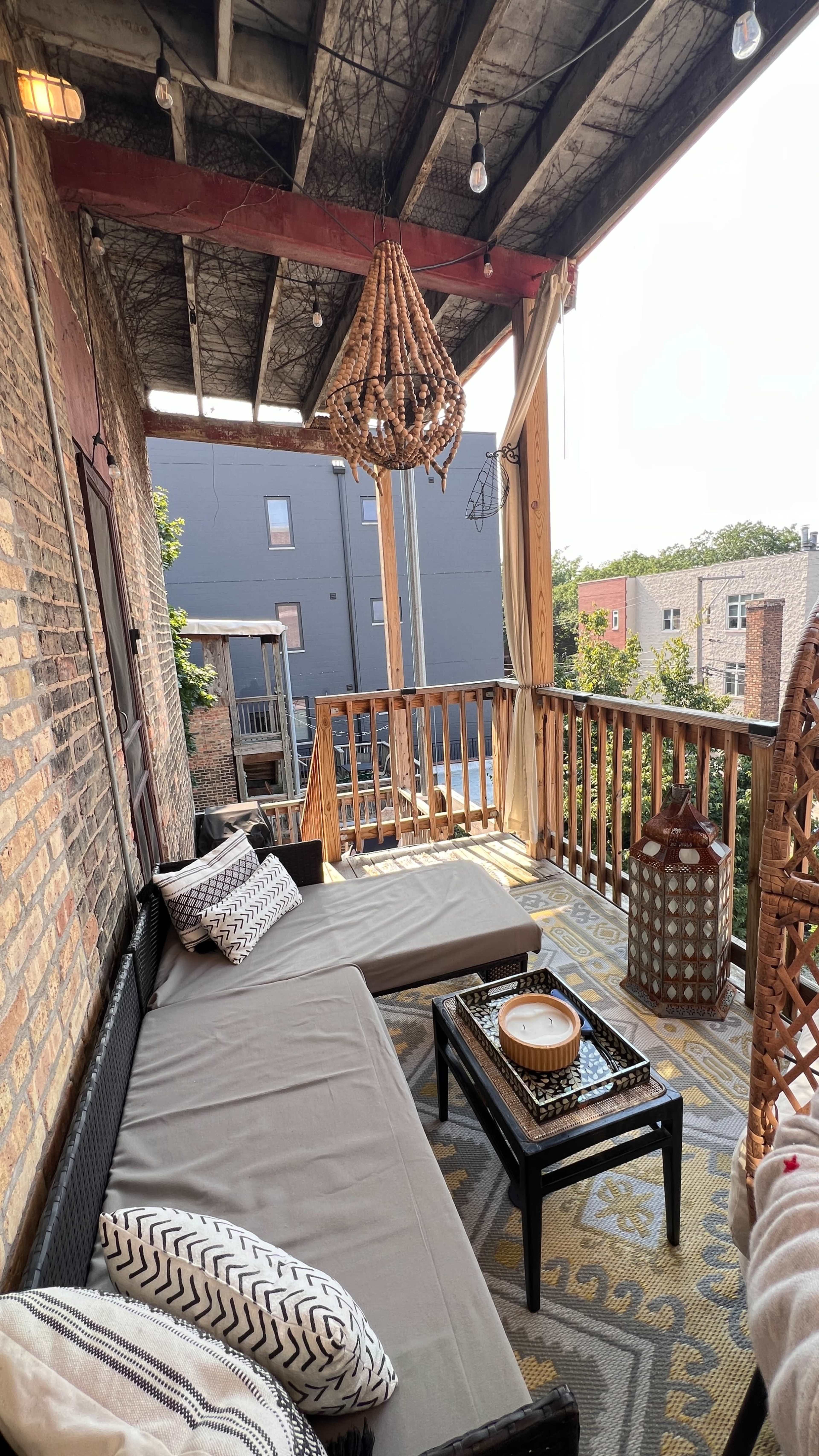 A covered balcony with a wicker seating area, a decorative lantern, and a woven light fixture hanging from the ceiling.
