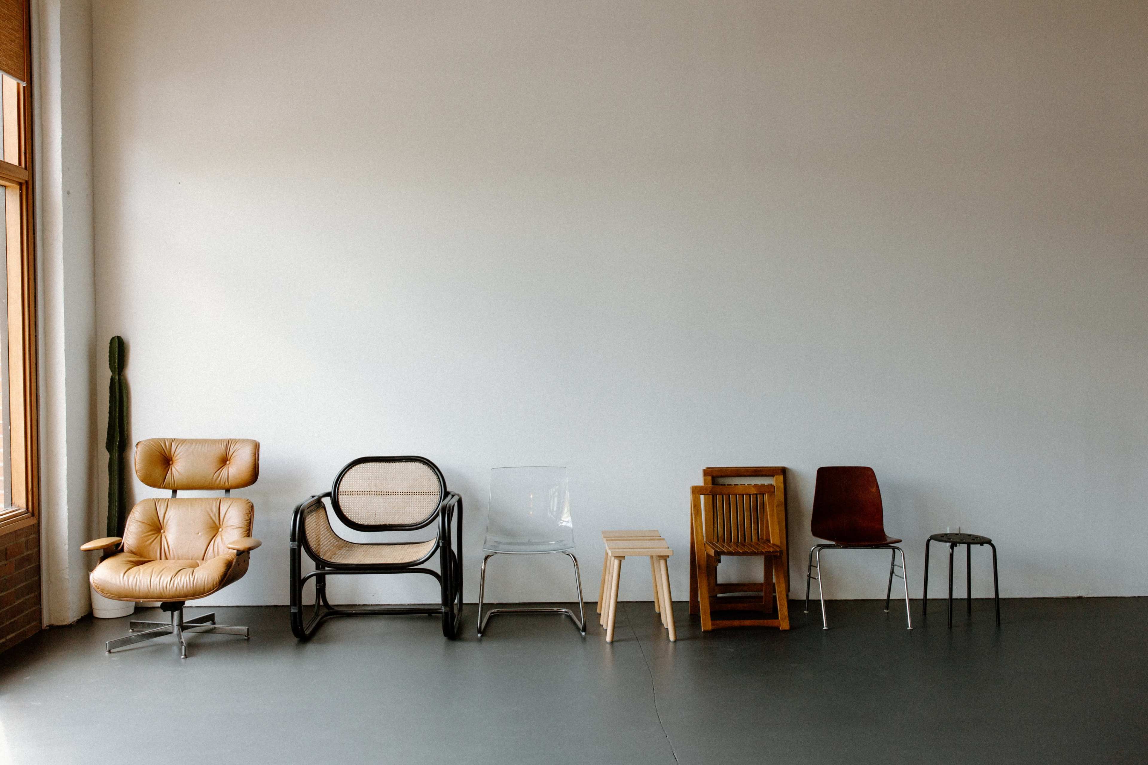 A row of various styled chairs is lined up against a blank wall.