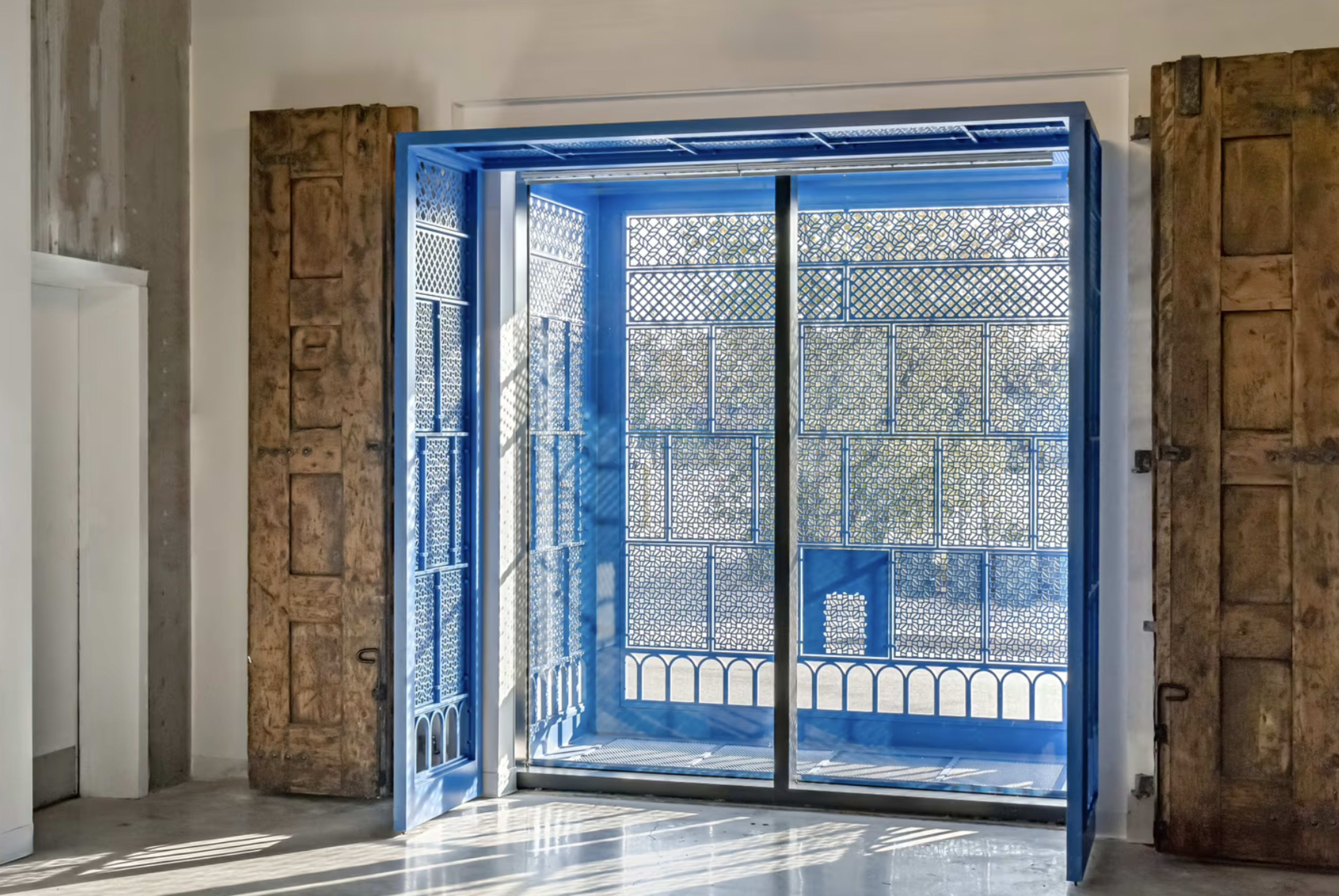 A large blue door with intricate ironwork is open, revealing a bright, sunlit courtyard beyond.