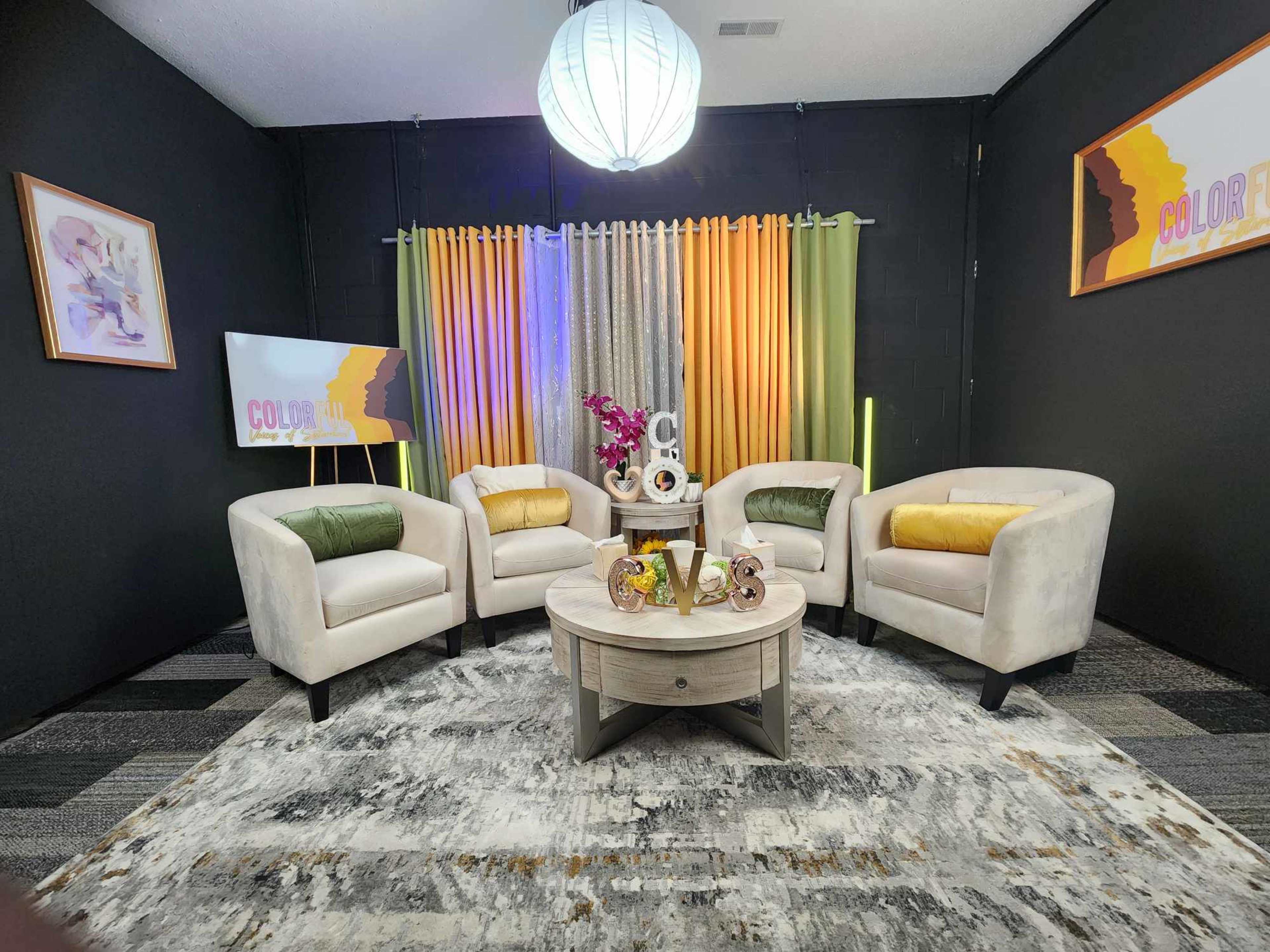 A modern living room setup featuring four beige chairs arranged around a circular coffee table, with colorful curtains and a decorative backdrop.