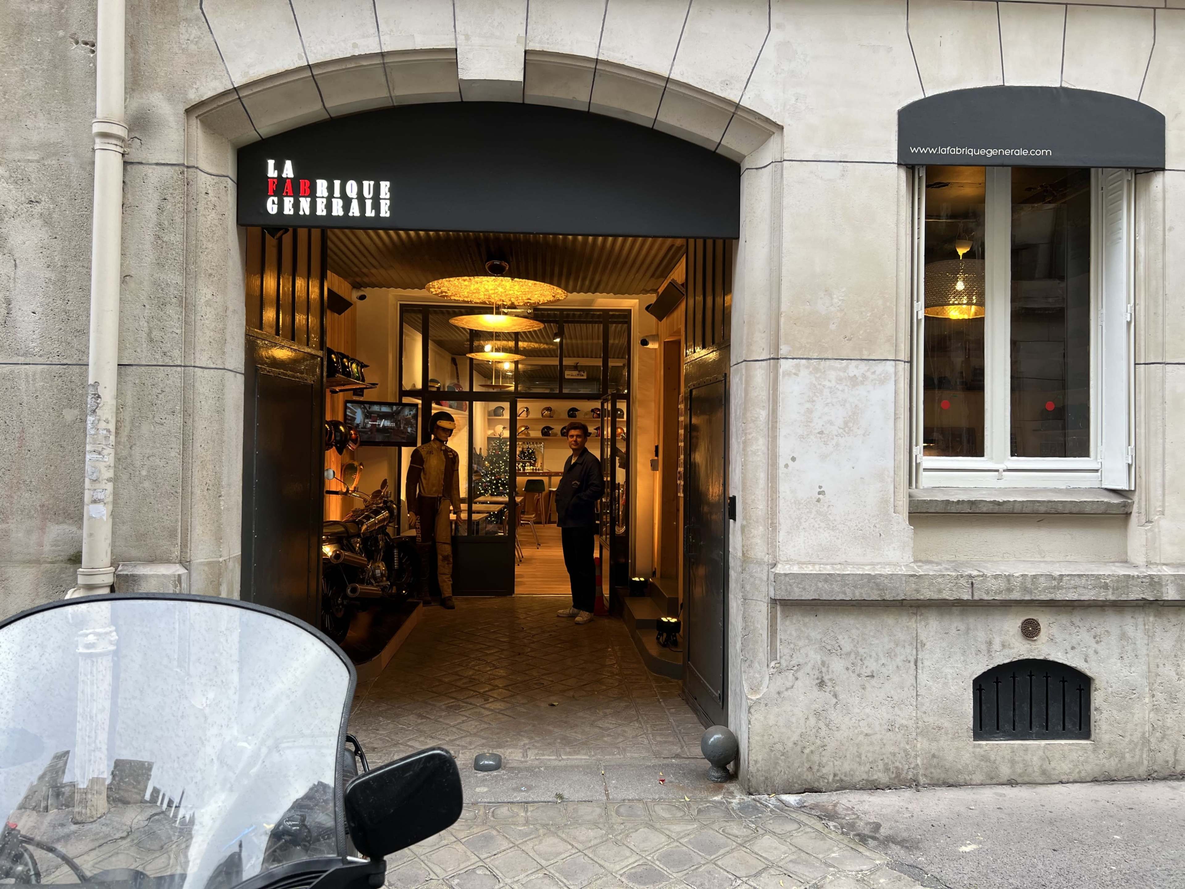 The entrance of a boutique named "La Fabrique Générale" is visible, showcasing a modern interior with customers inside and a motorcycle parked in front.