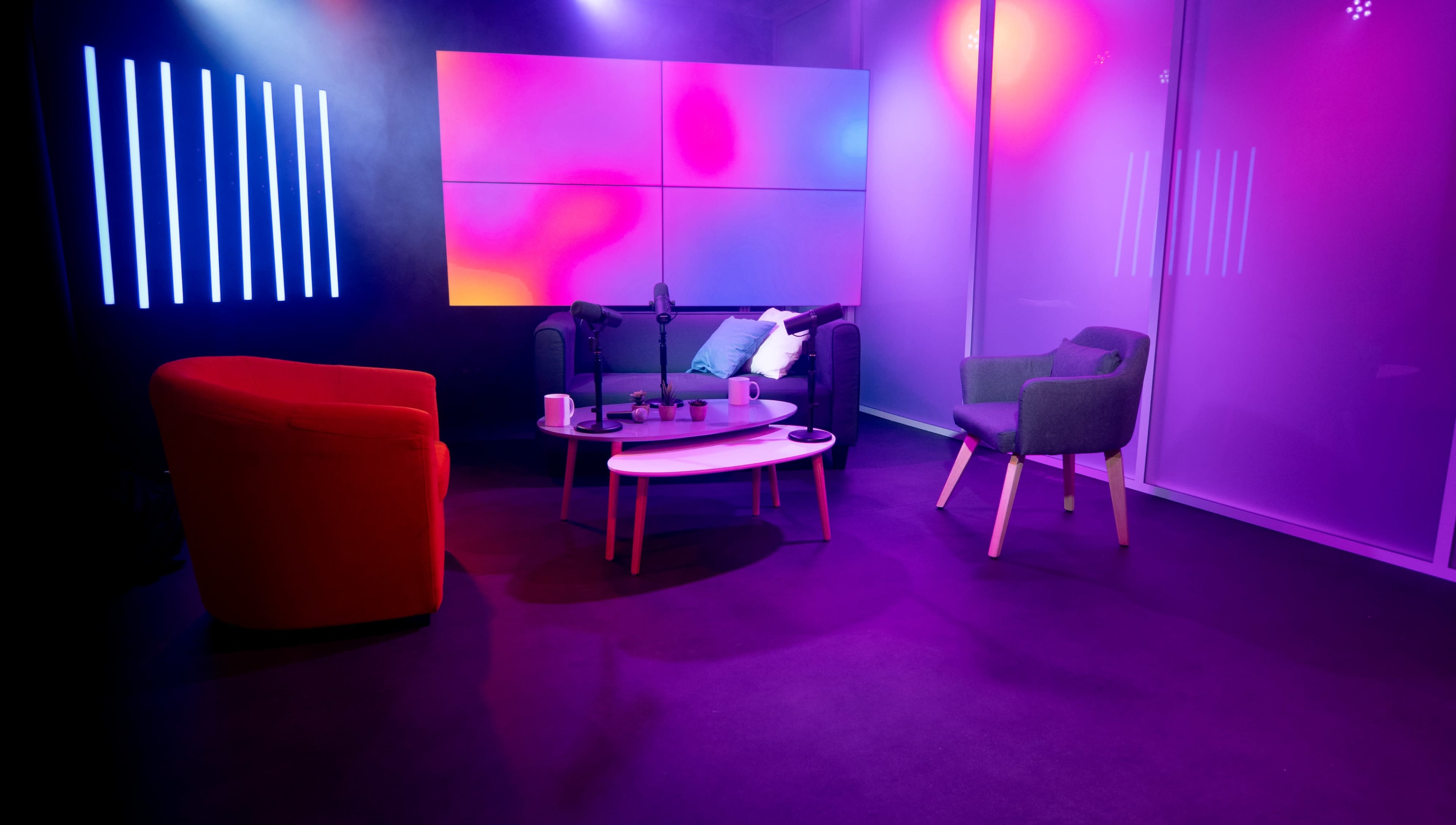 A modern seating area featuring two chairs and a coffee table, illuminated by colorful ambient lights and surrounded by a backdrop of large panels.