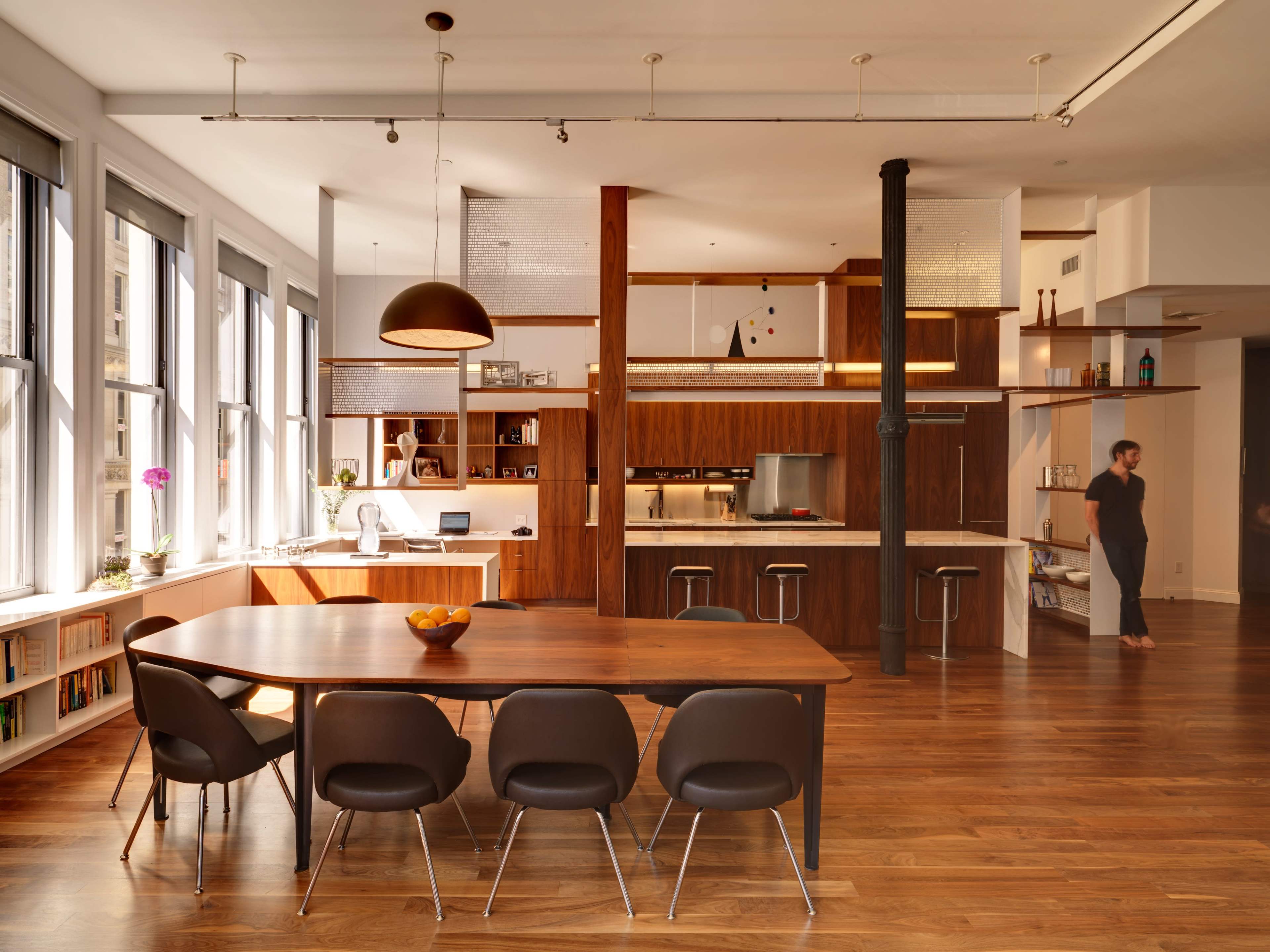The image shows a modern open-concept kitchen and dining area with a large wooden table, dark chairs, and a mix of wooden cabinetry and countertops.