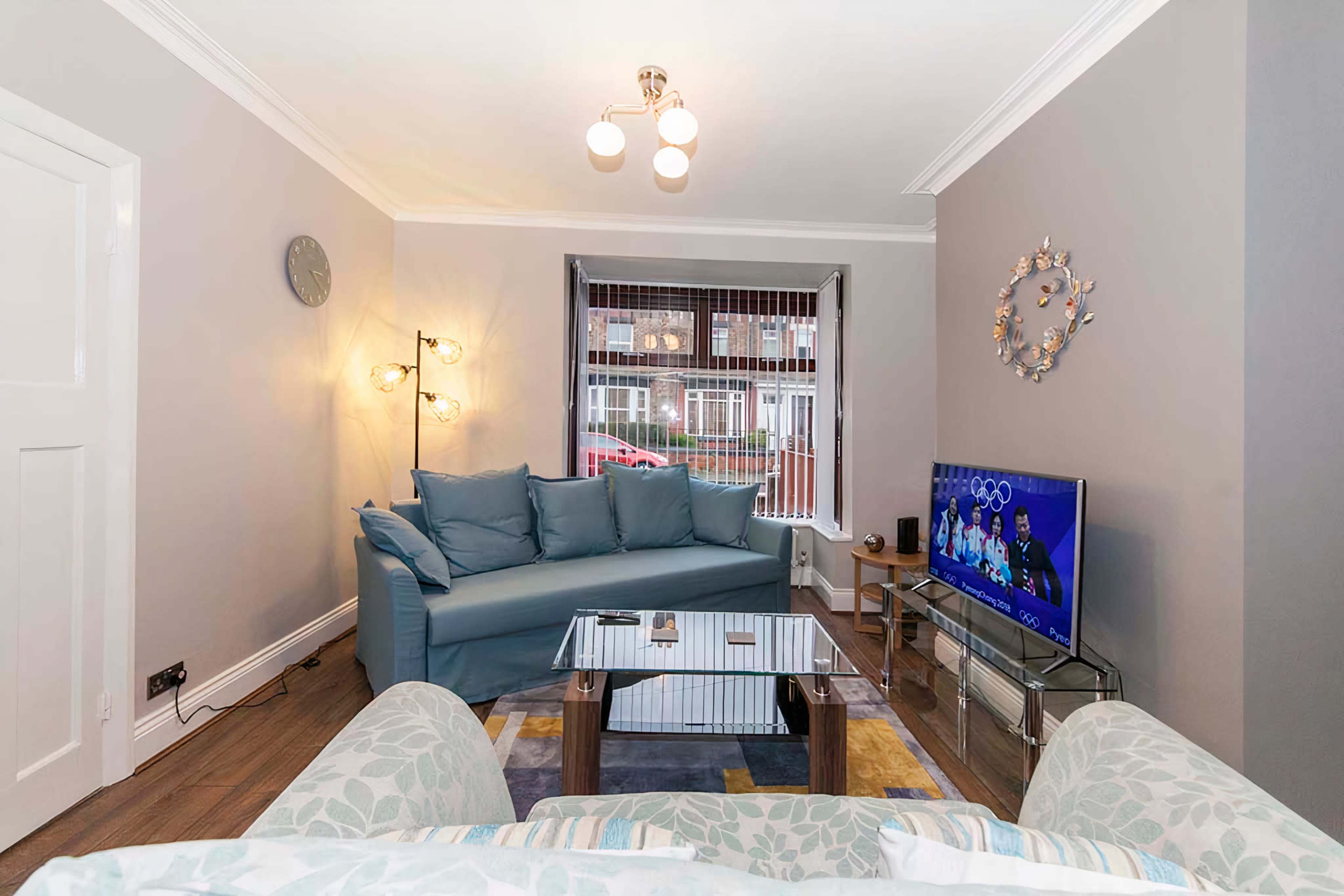 A furnished living room with a blue sofa, a glass coffee table, and a television displaying a program.
