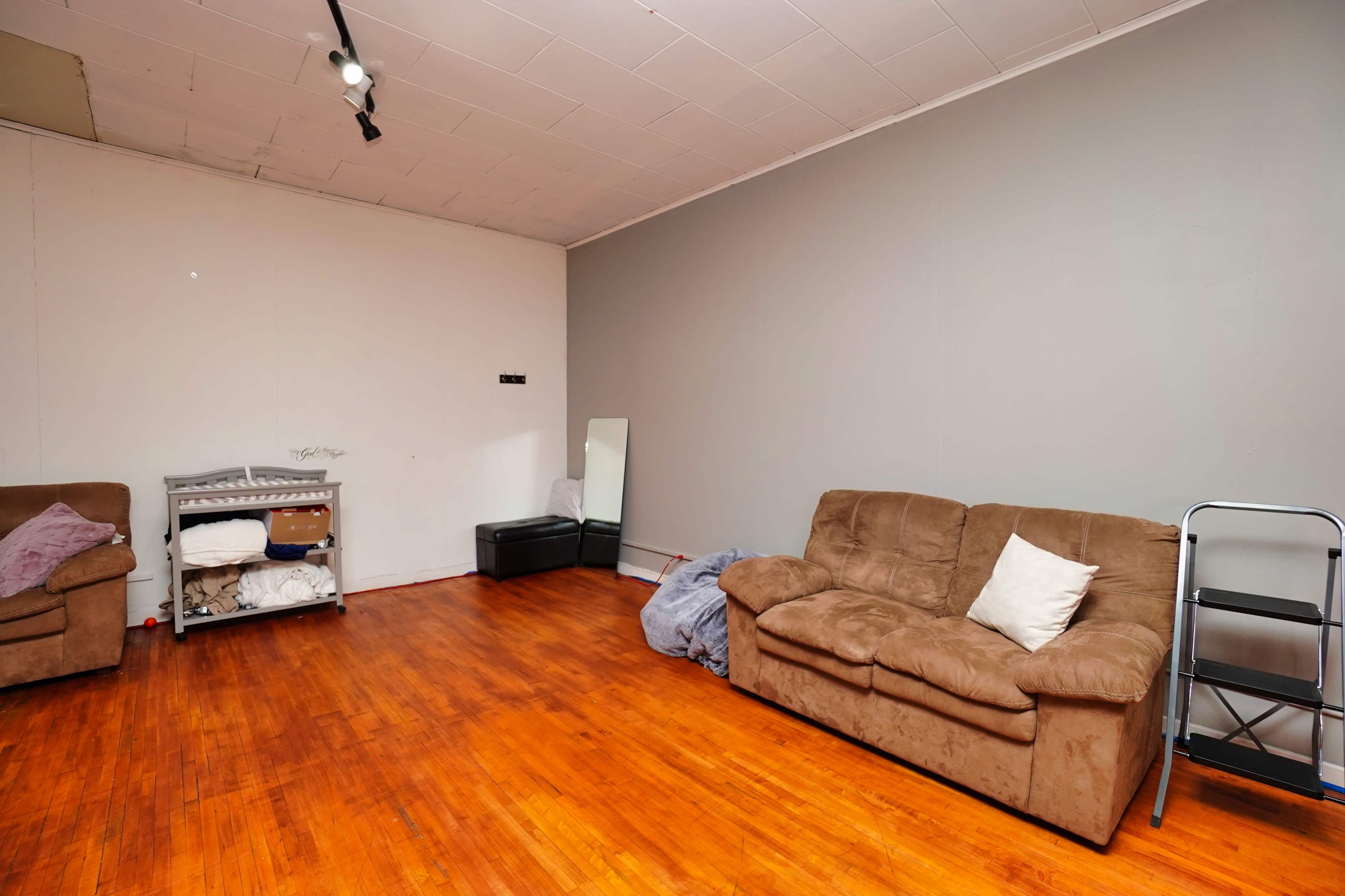 The room features brown couches, a mirror, a shelving unit, and wood flooring, with minimal decor and furniture.
