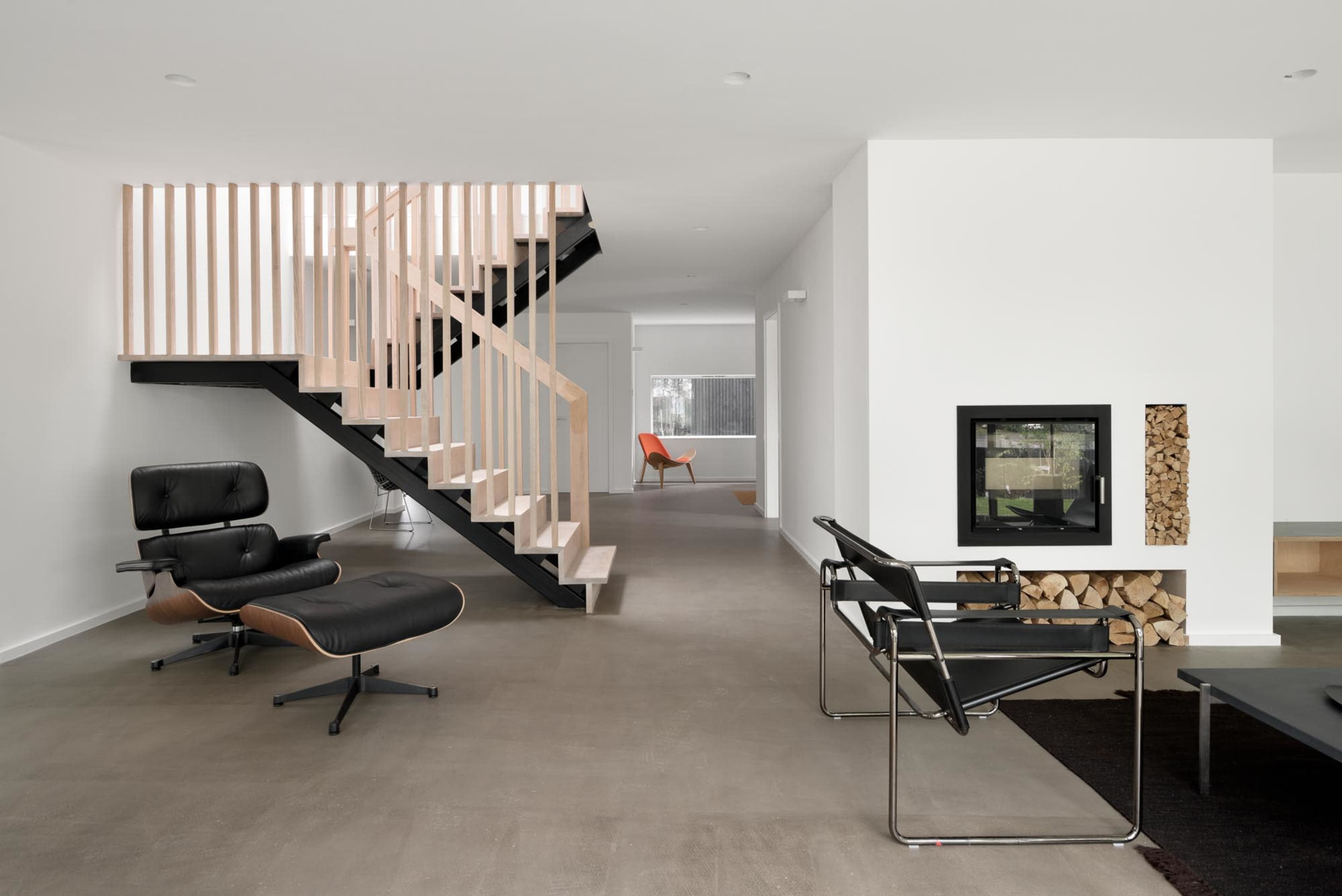 A modern interior with a staircase featuring wooden railings, a black armchair, and a fireplace integrated into a white wall.