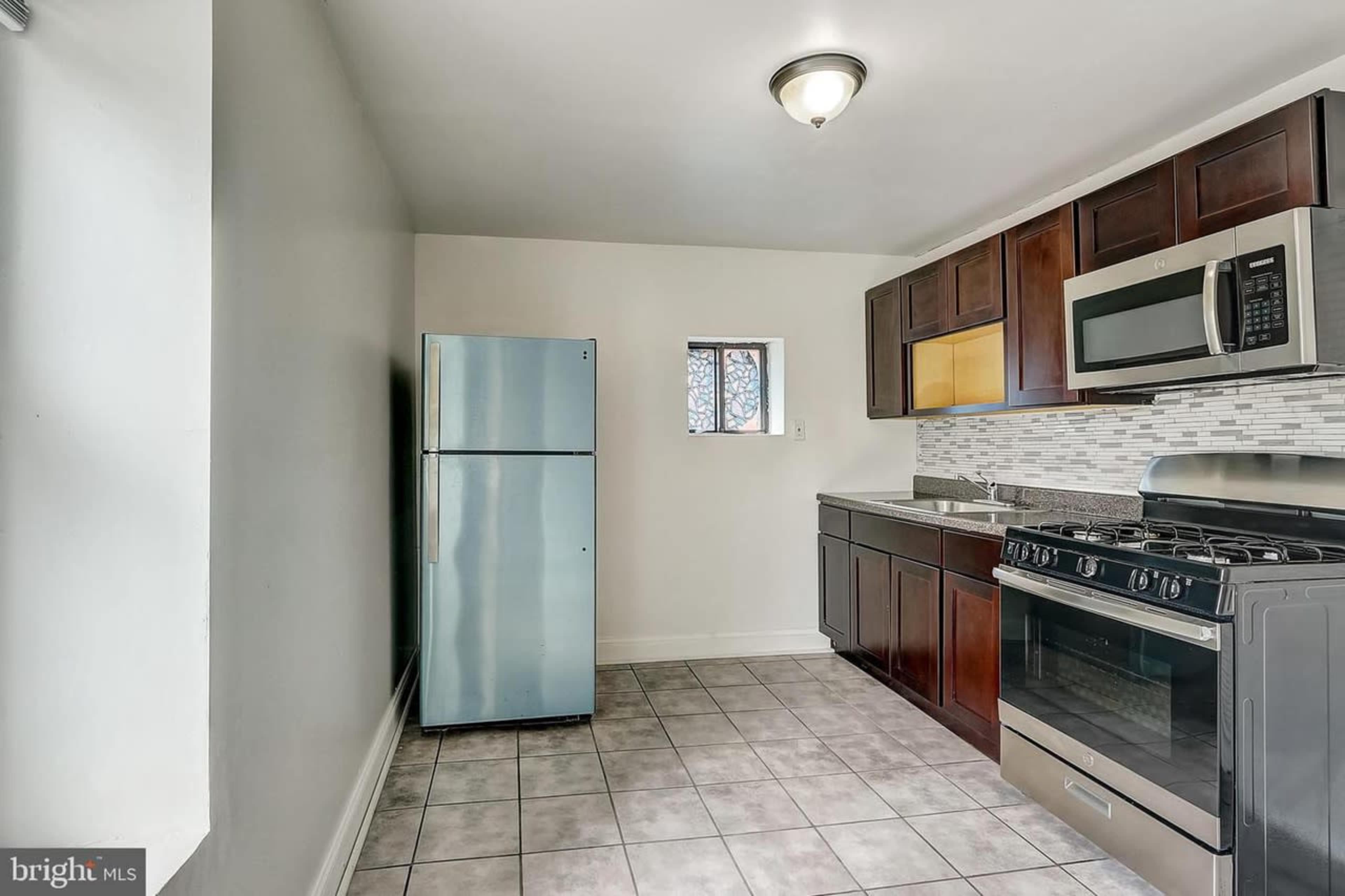 A kitchen featuring dark wood cabinetry, stainless steel appliances, and tiled flooring.