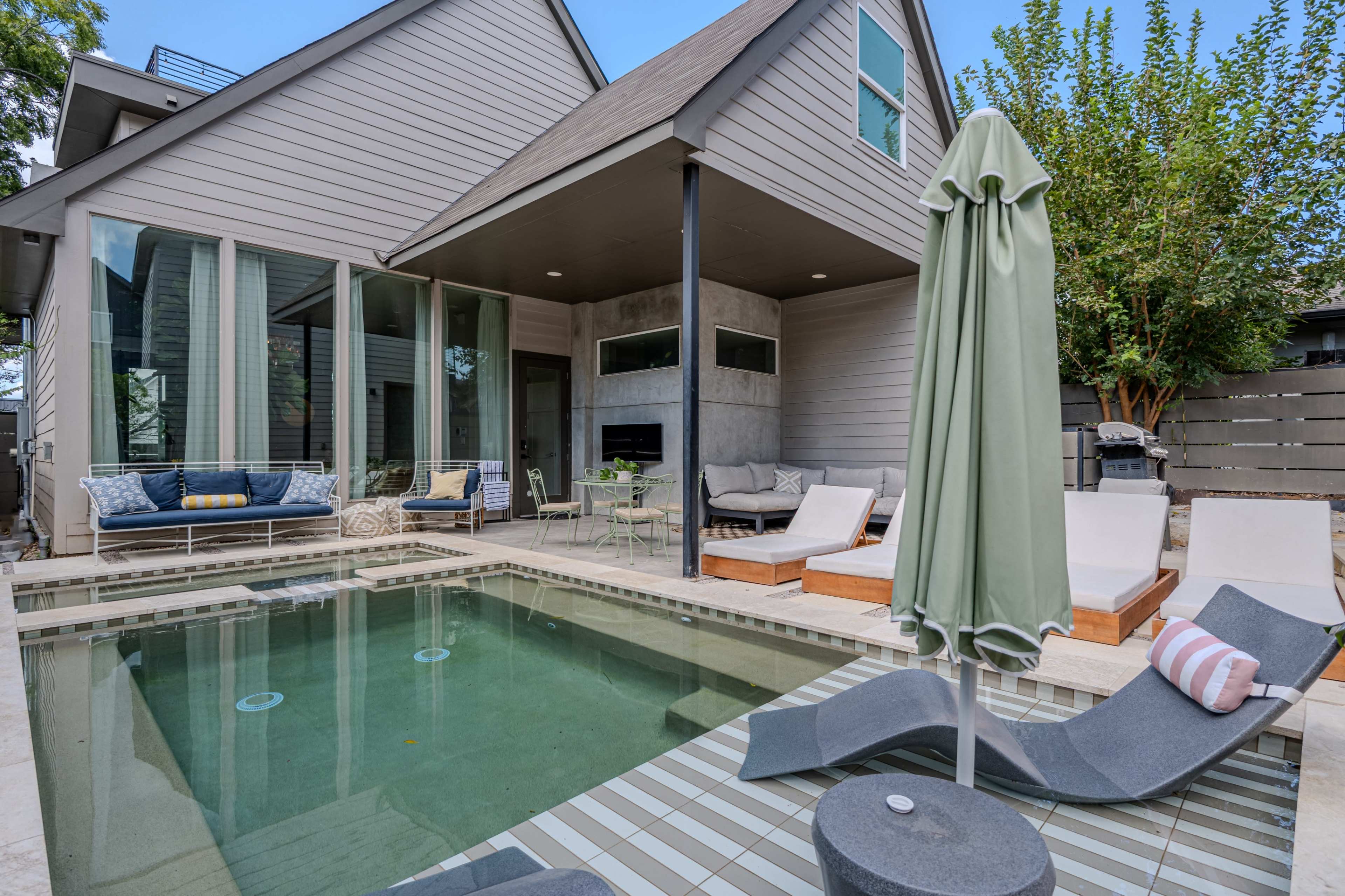 The image shows a modern patio area featuring a small pool, lounge chairs, and an outdoor seating arrangement adjacent to a house.