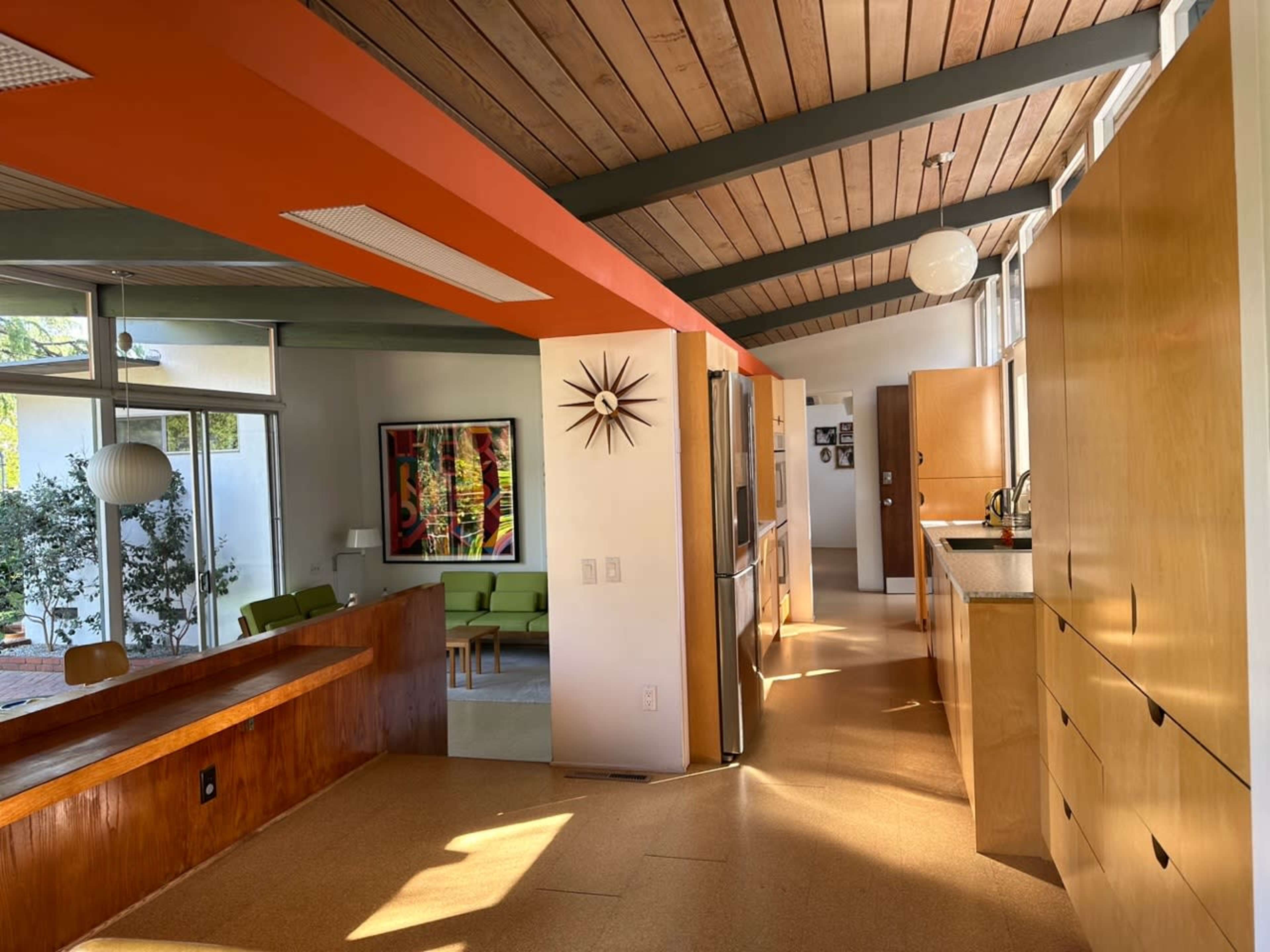 A modern interior space with wooden ceilings, an open layout, and kitchen areas featuring wood cabinets and bright orange accents.