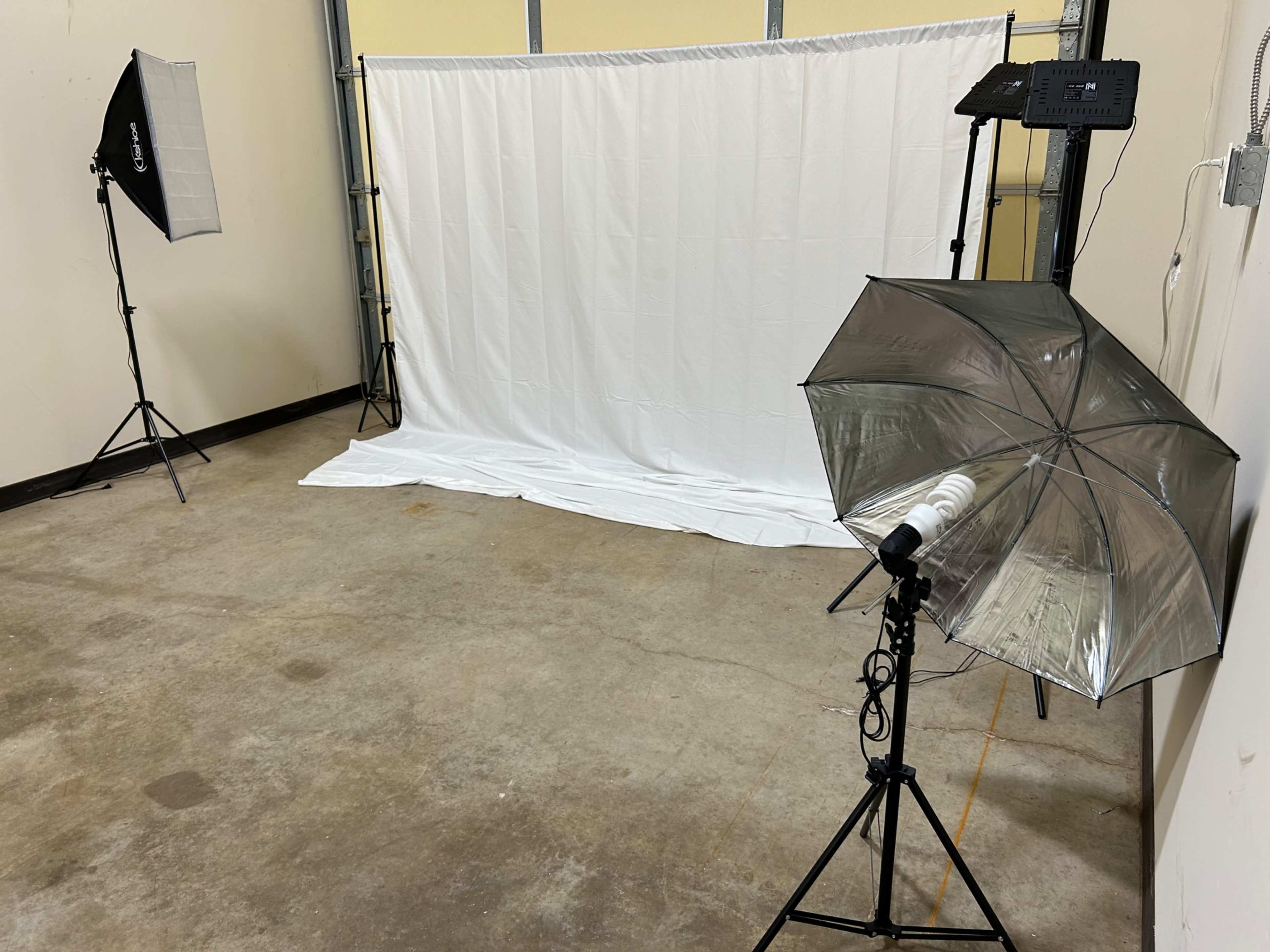 The image shows a photography setup with a white backdrop and two lighting umbrellas positioned in a sparsely furnished room.