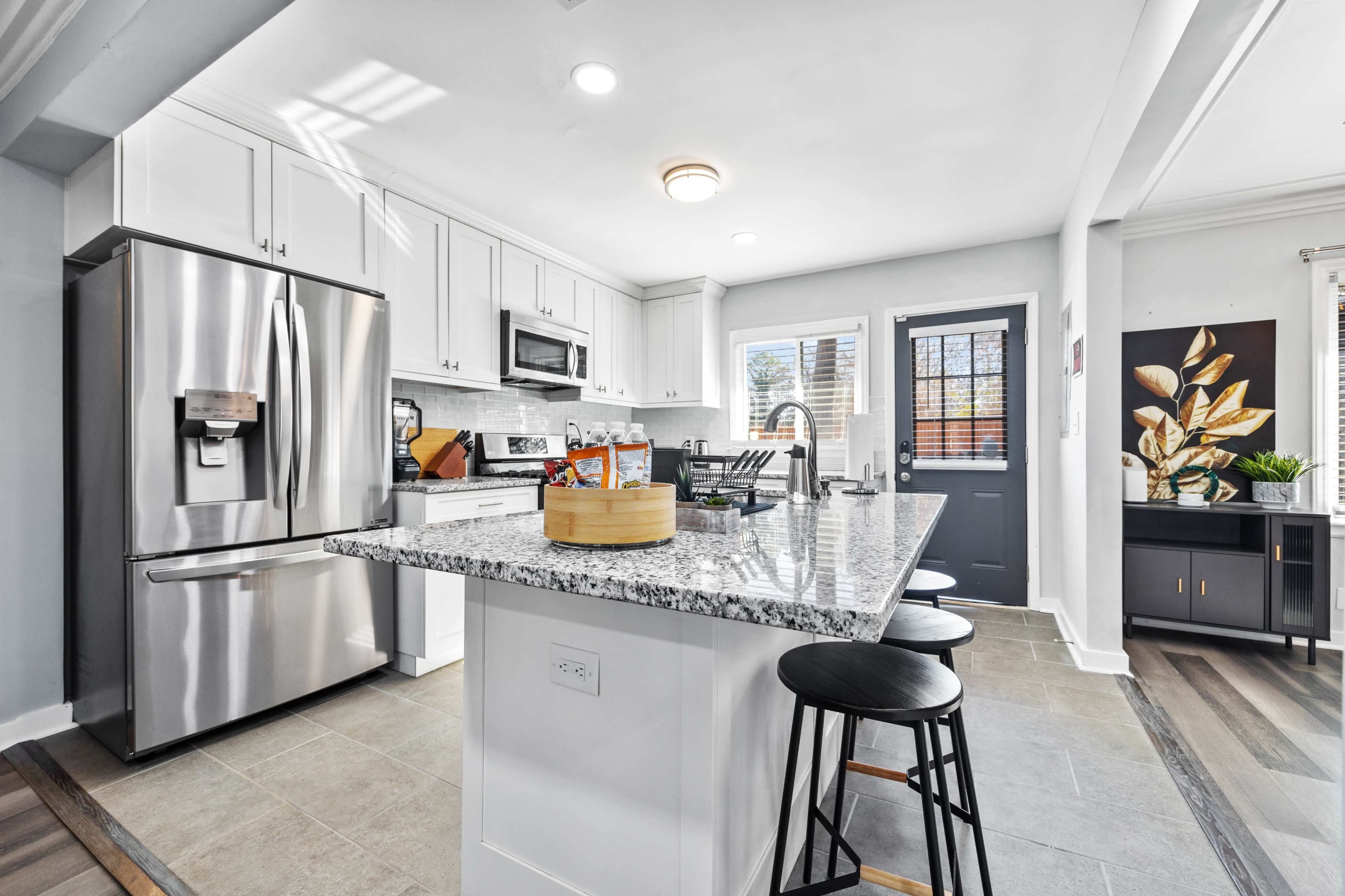 A modern kitchen features stainless steel appliances, a spacious island with bar stools, and light-colored cabinetry.