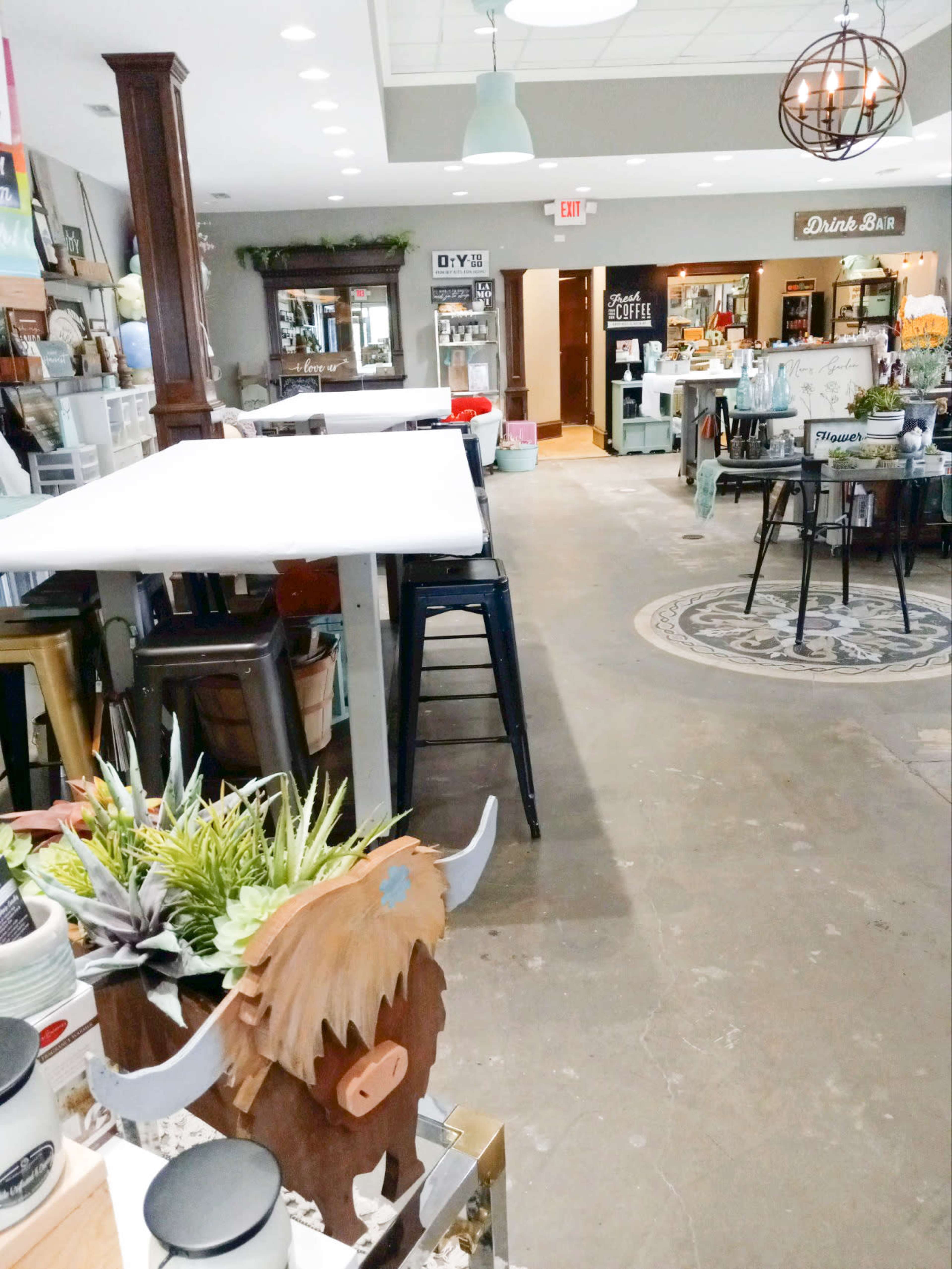 A spacious interior of a boutique featuring tables, decorative plants, and a drink bar with various items displayed along the walls.