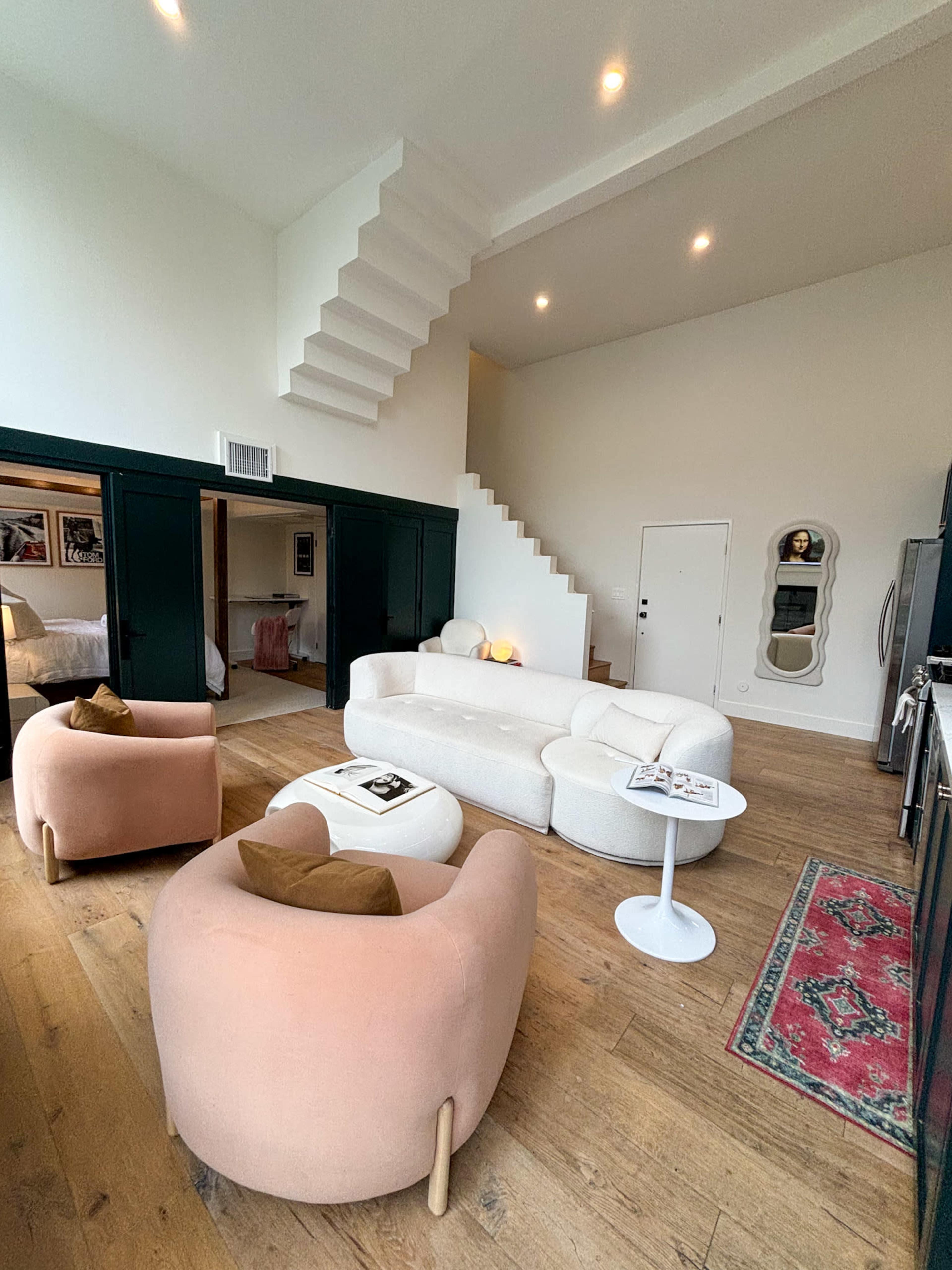 A modern living room with two rounded seating chairs, a low table, and a staircase leading to an upper level, all set against a white and dark green color scheme.