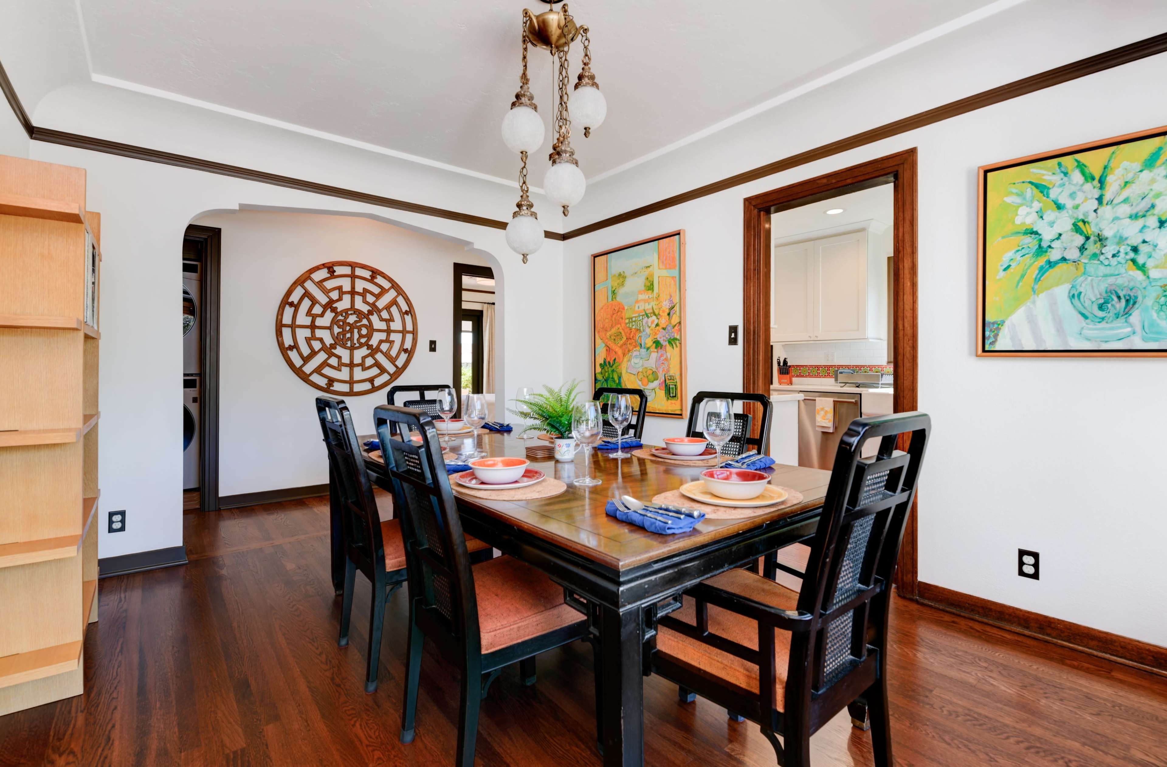 A dining room features a large table surrounded by black chairs, with decorative artwork on the walls and a light fixture hanging from the ceiling.