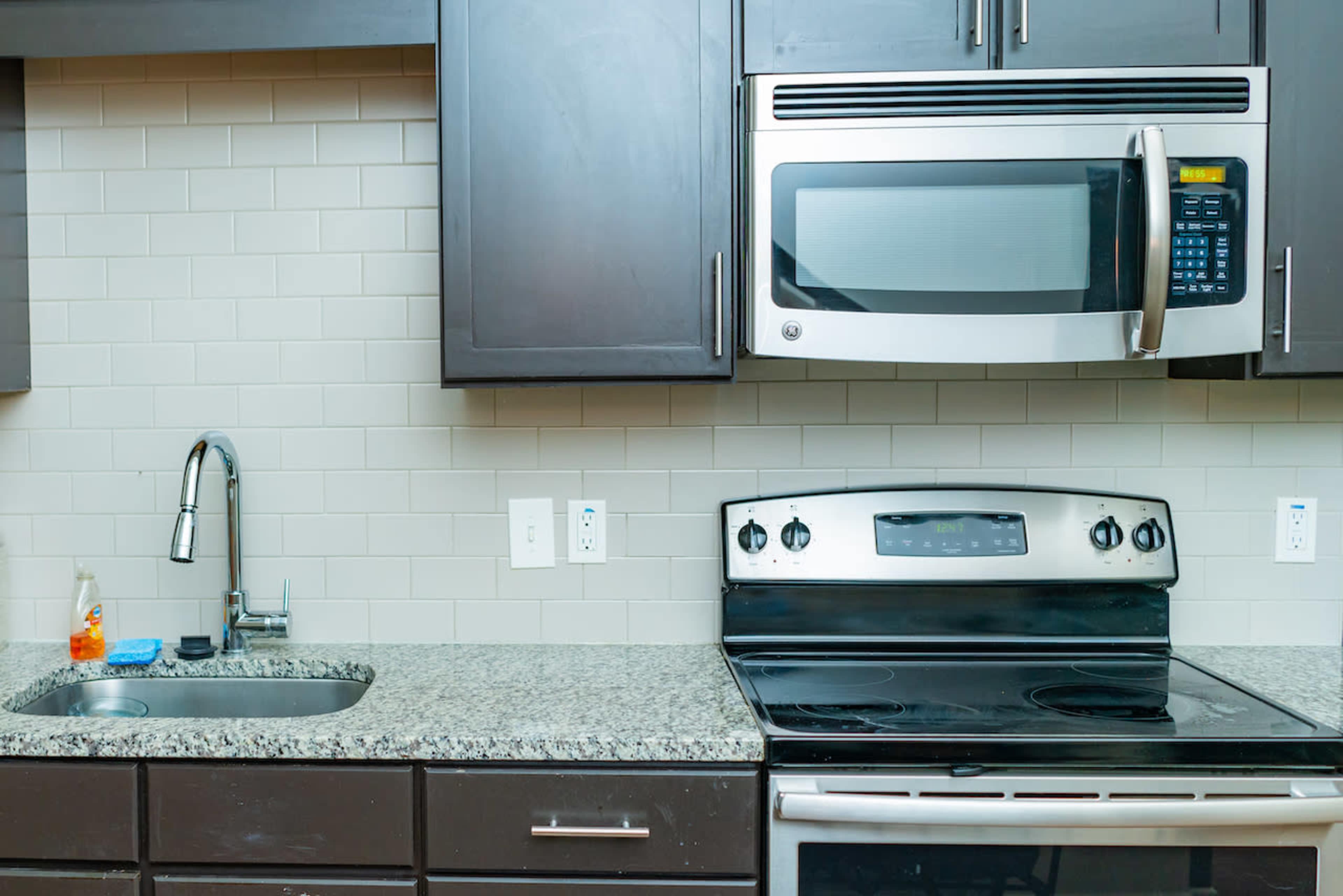 A kitchen with dark cabinets, a stainless steel microwave above a black stove, and a granite countertop with a sink.