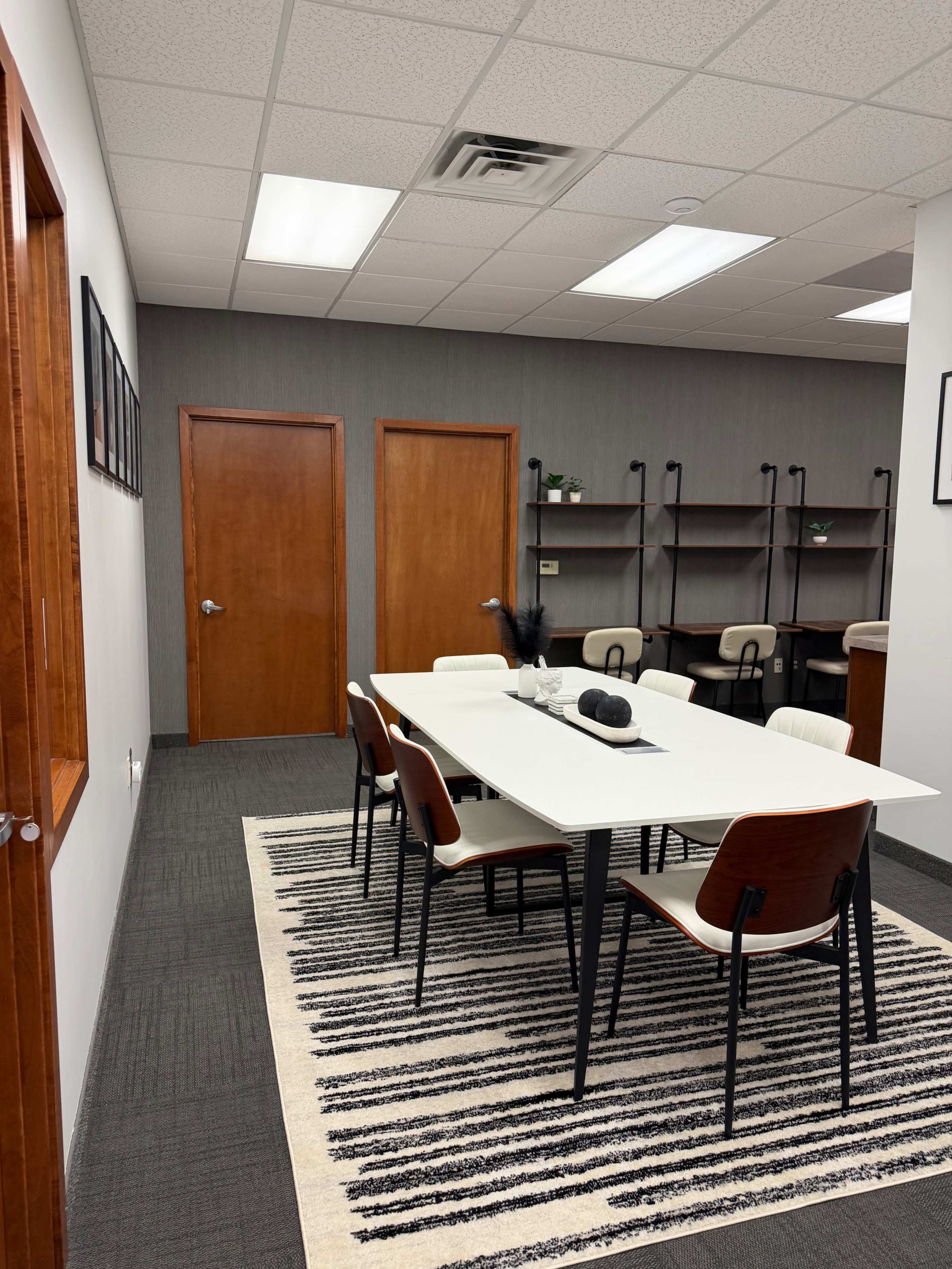 The image shows a modern conference room with a white table and six chairs, flanked by two wooden doors and shelves on the walls.