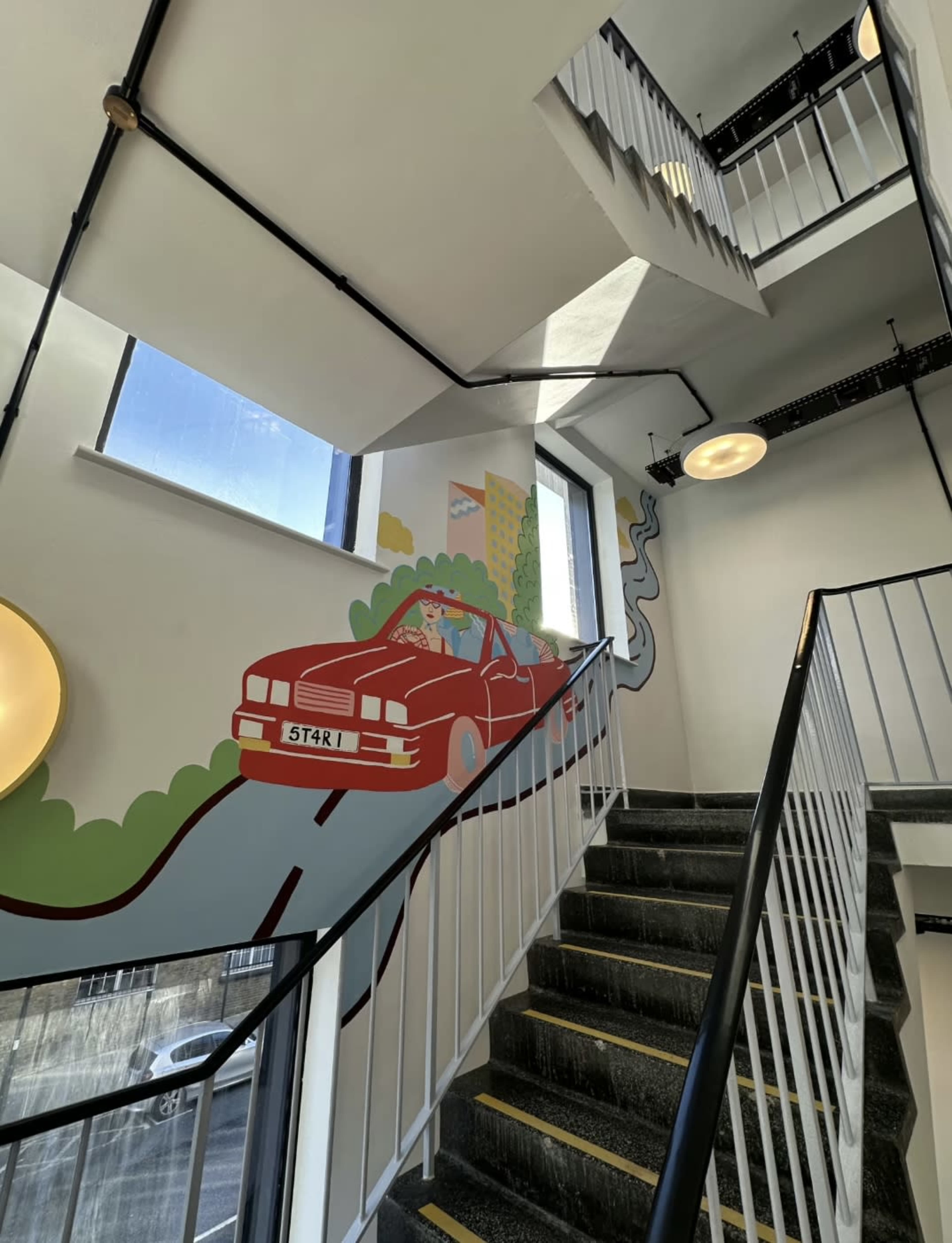 A staircase features a mural of a red car driving through a scenic landscape alongside the walls.