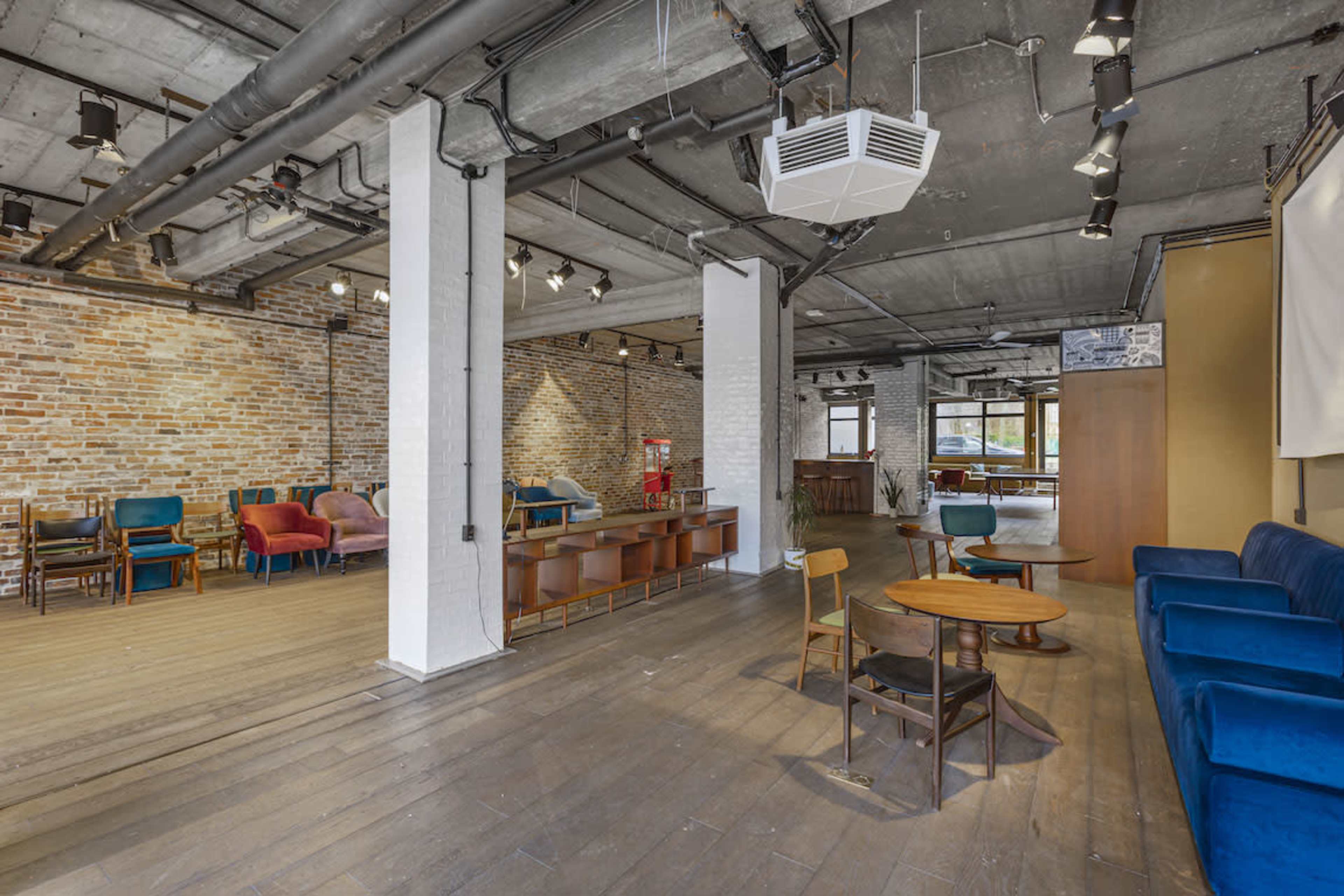 A spacious interior with a mix of seating areas, featuring brick walls, wooden flooring, and various types of furniture arranged in an open layout.