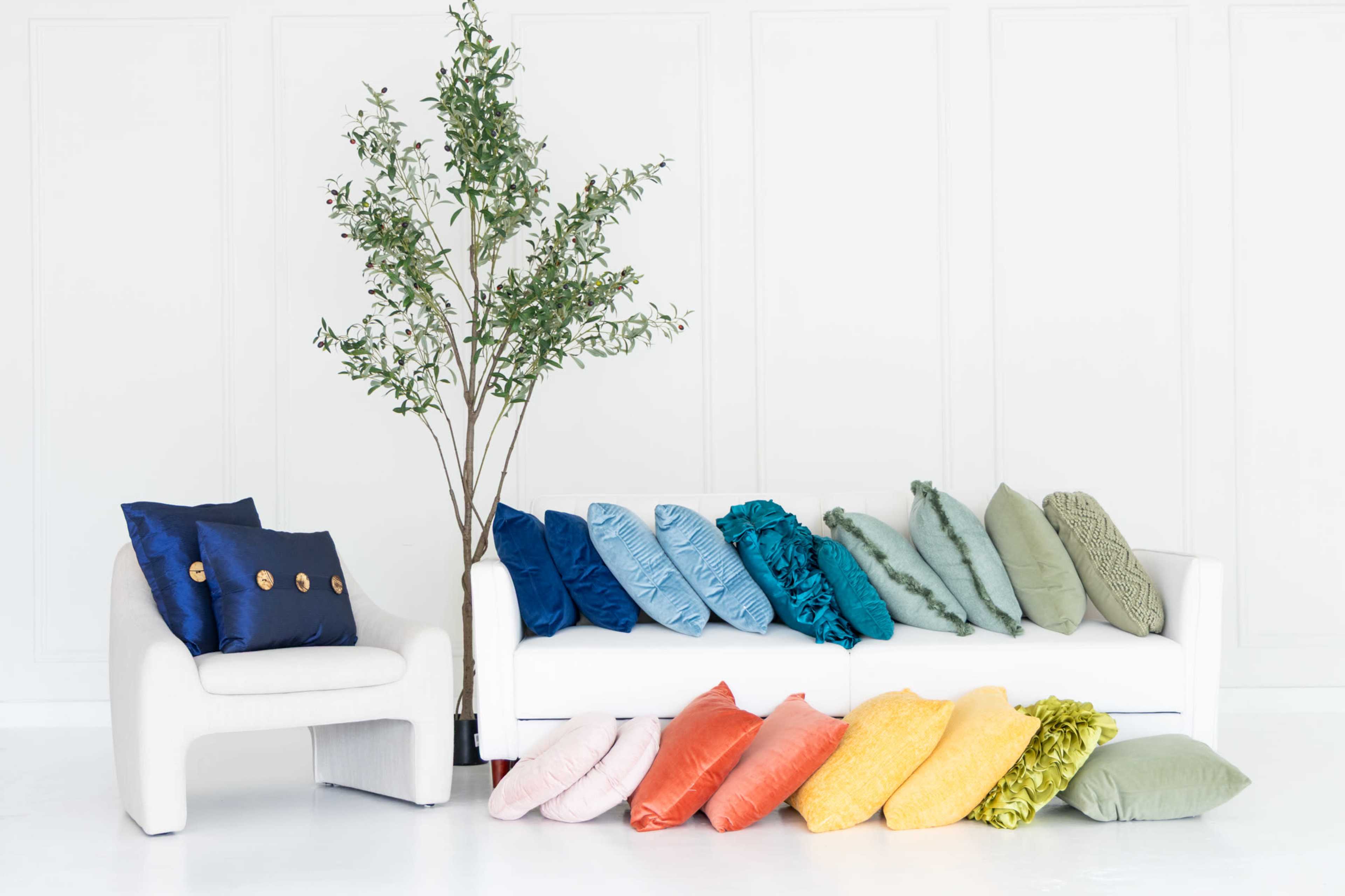 A modern white sofa is adorned with a variety of colorful decorative pillows, while a potted plant stands beside a nearby chair.