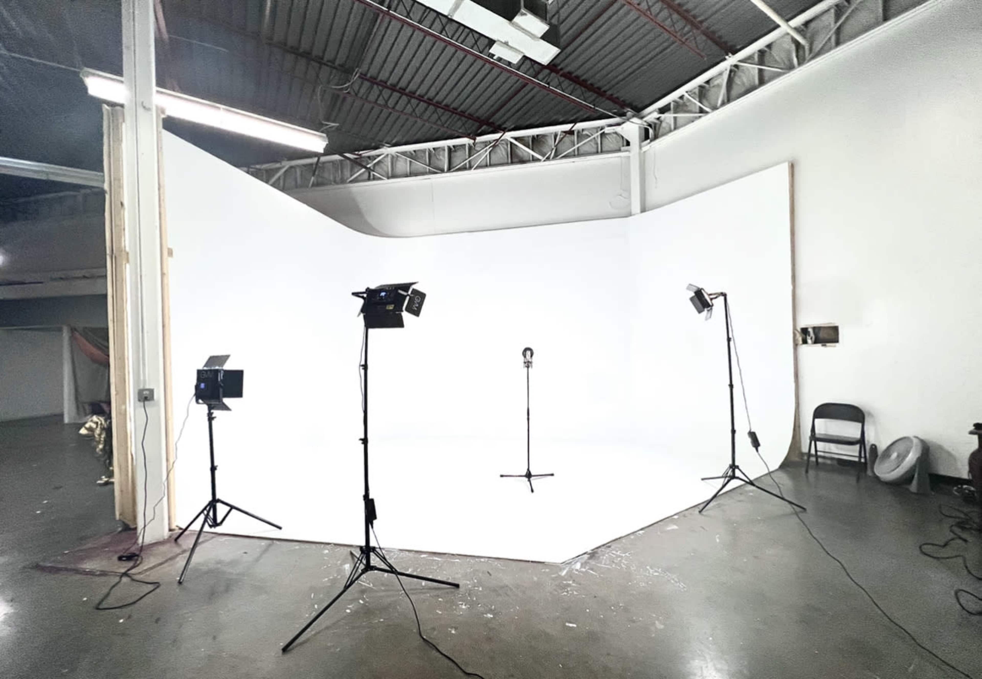A photography studio is set up with a seamless white backdrop and several lights positioned around a microphone stand.