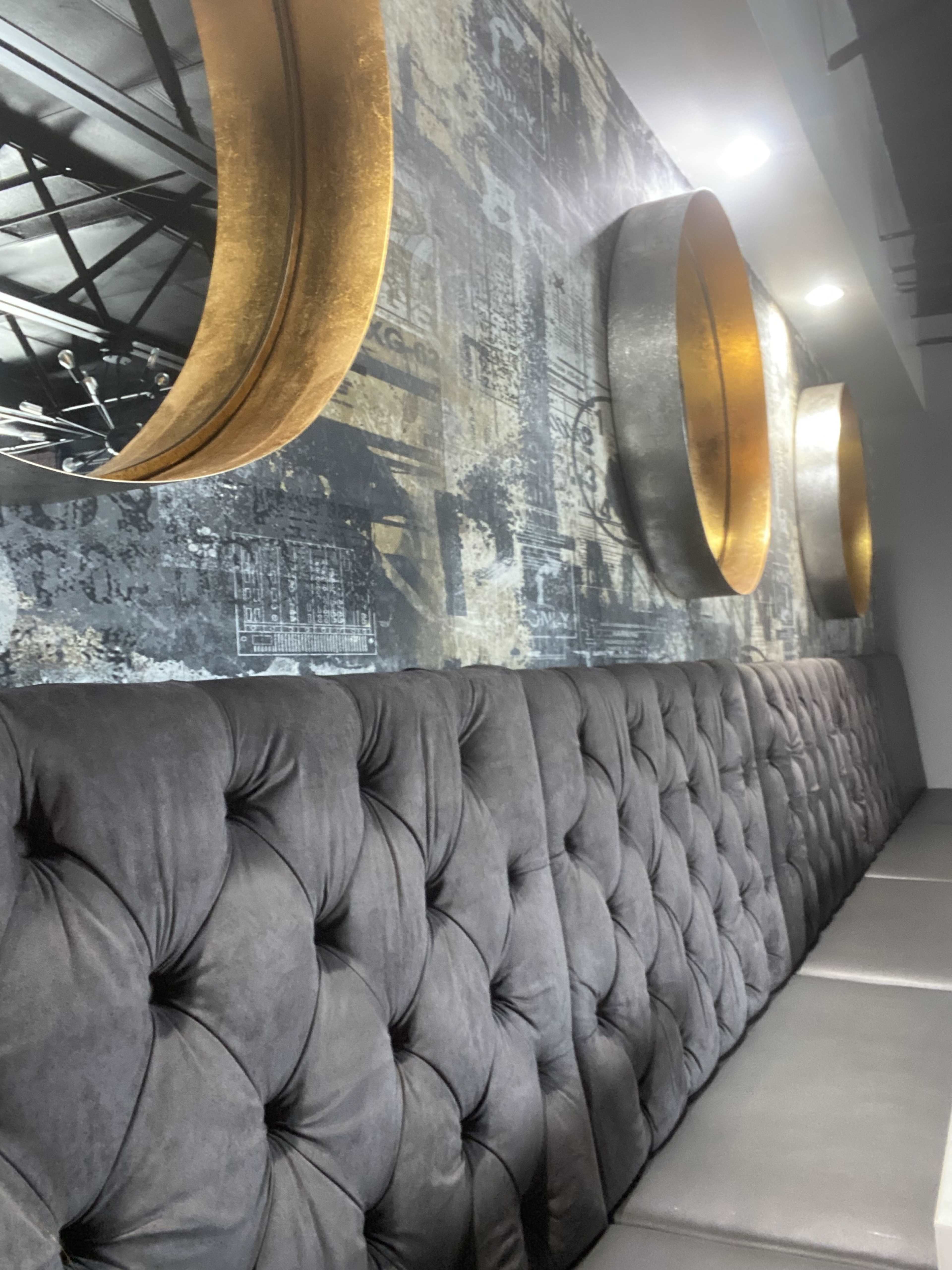 The image shows a upholstered gray banquette against a textured wall featuring circular metal wall decorations.