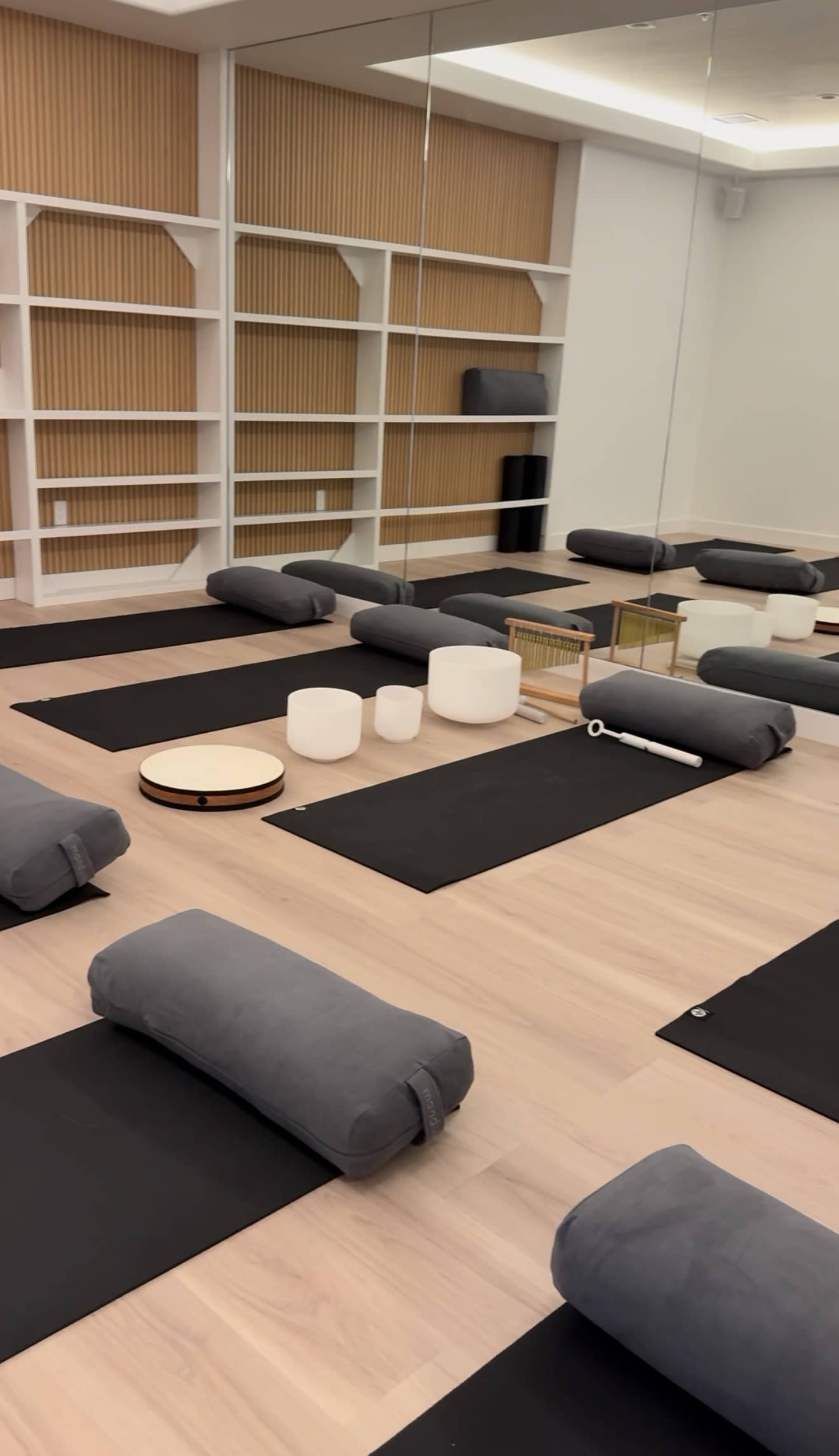 The image shows a yoga or meditation studio with several mats, bolsters, and props neatly arranged in a spacious room.