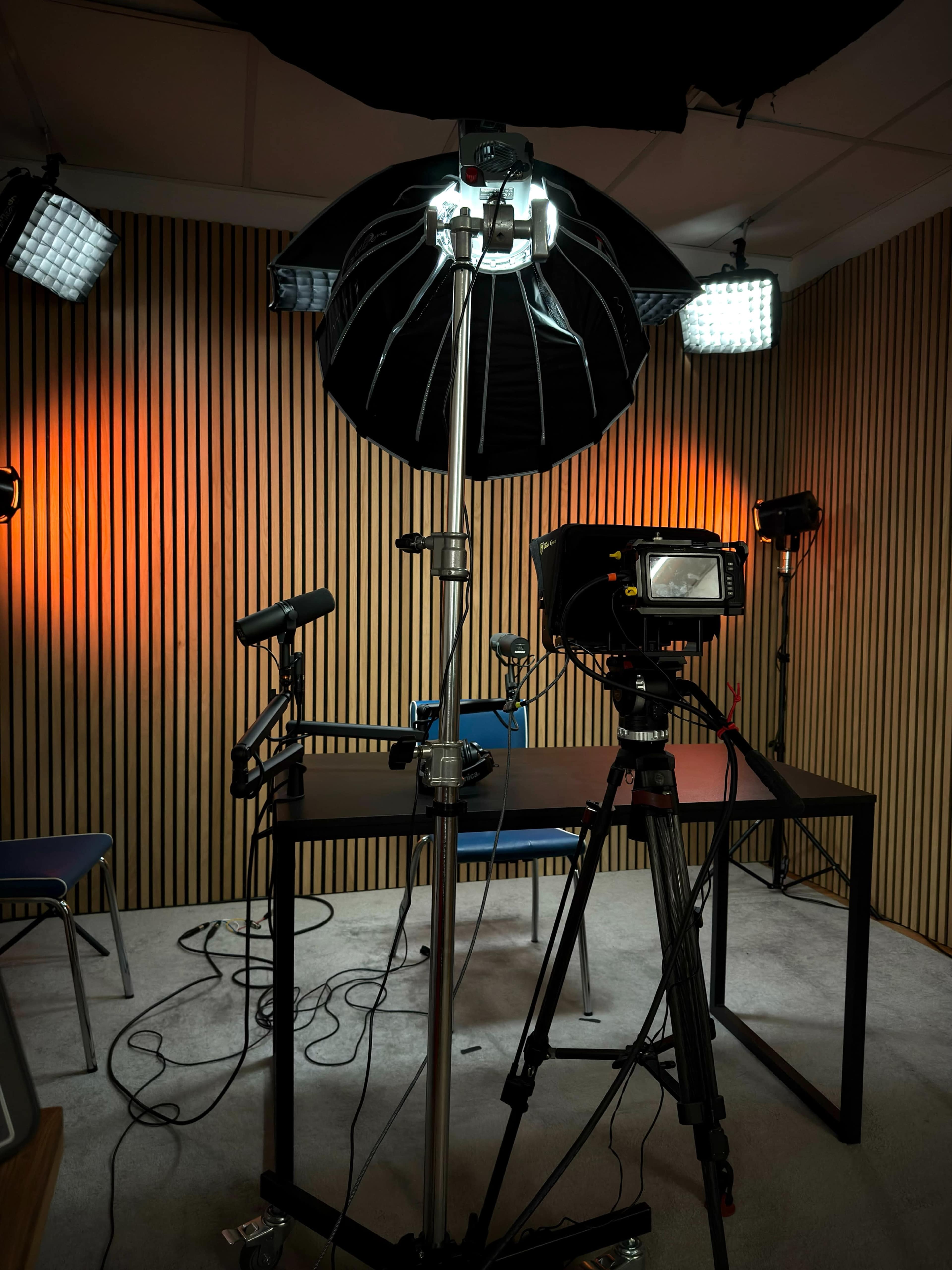 The image shows a photography setup in a studio with a camera on a tripod, lighting equipment, and a table and chairs arranged for a shoot.