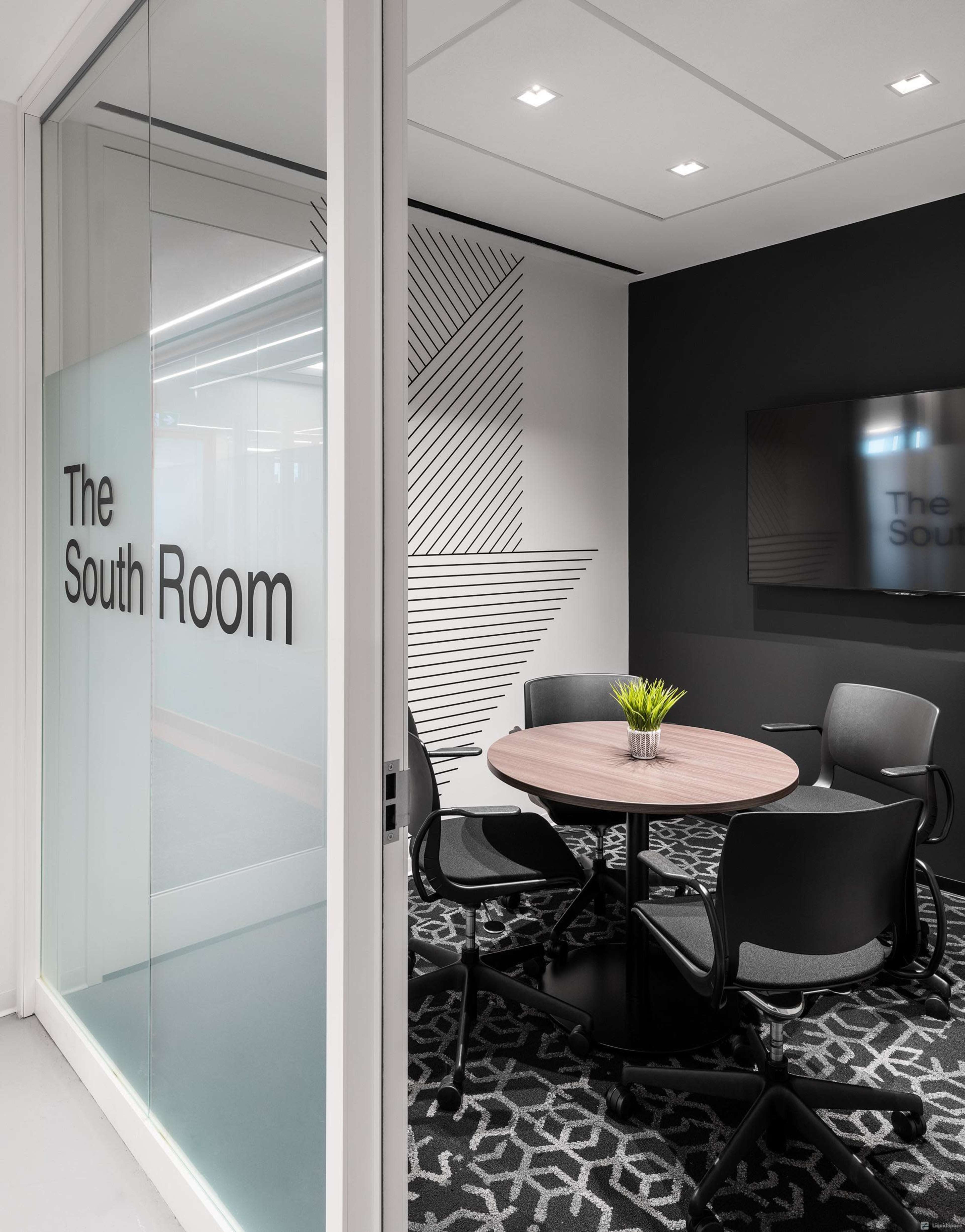 The image shows a modern conference room named "The South Room," featuring a round table with four chairs and a large display screen on the wall.