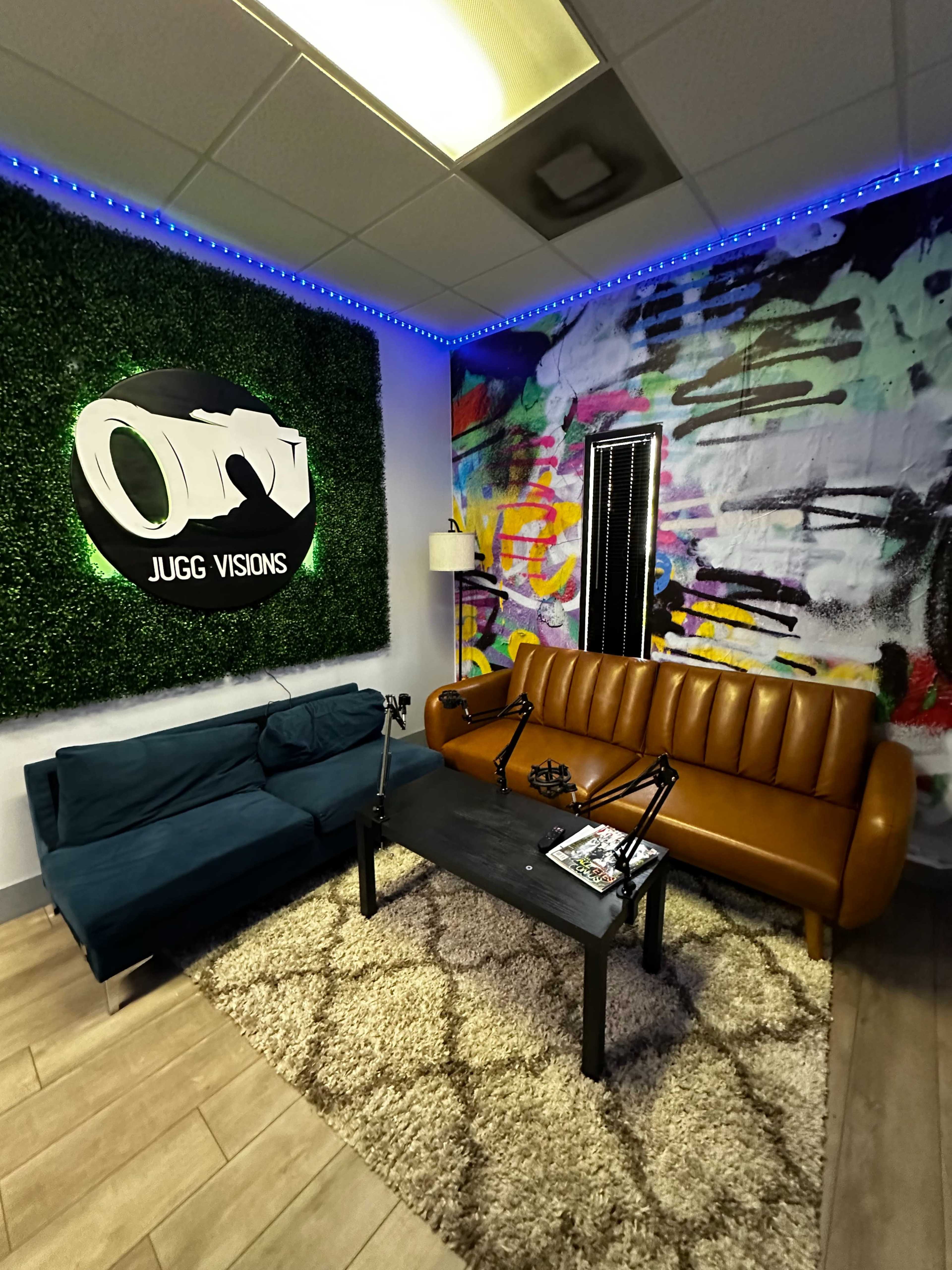 The image shows a modern and colorful lounge area with two sofas, a coffee table, and a wall adorned with green foliage and abstract art.