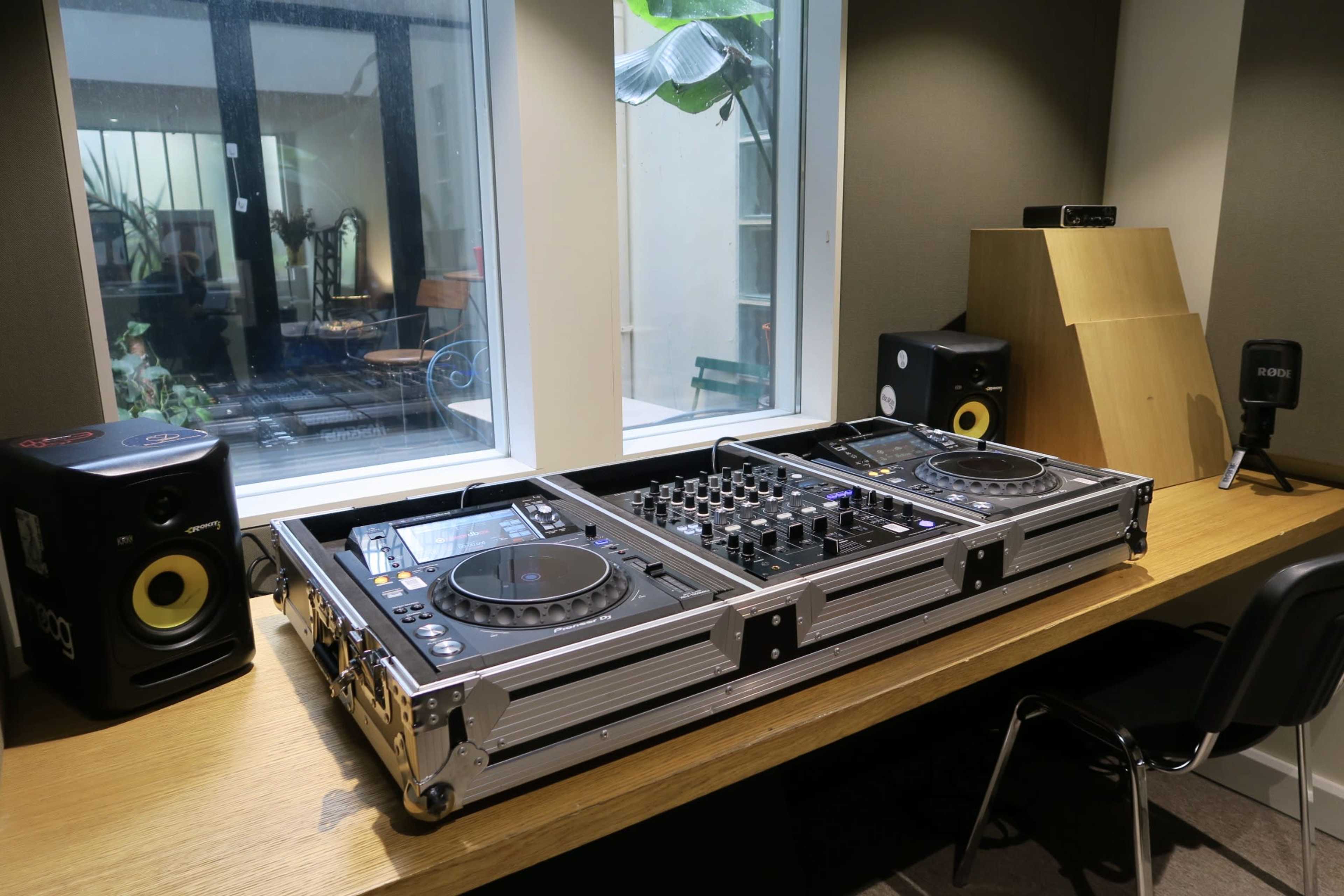 A large DJ setup is placed on a wooden table in a well-lit room with windows, featuring speakers on either side.