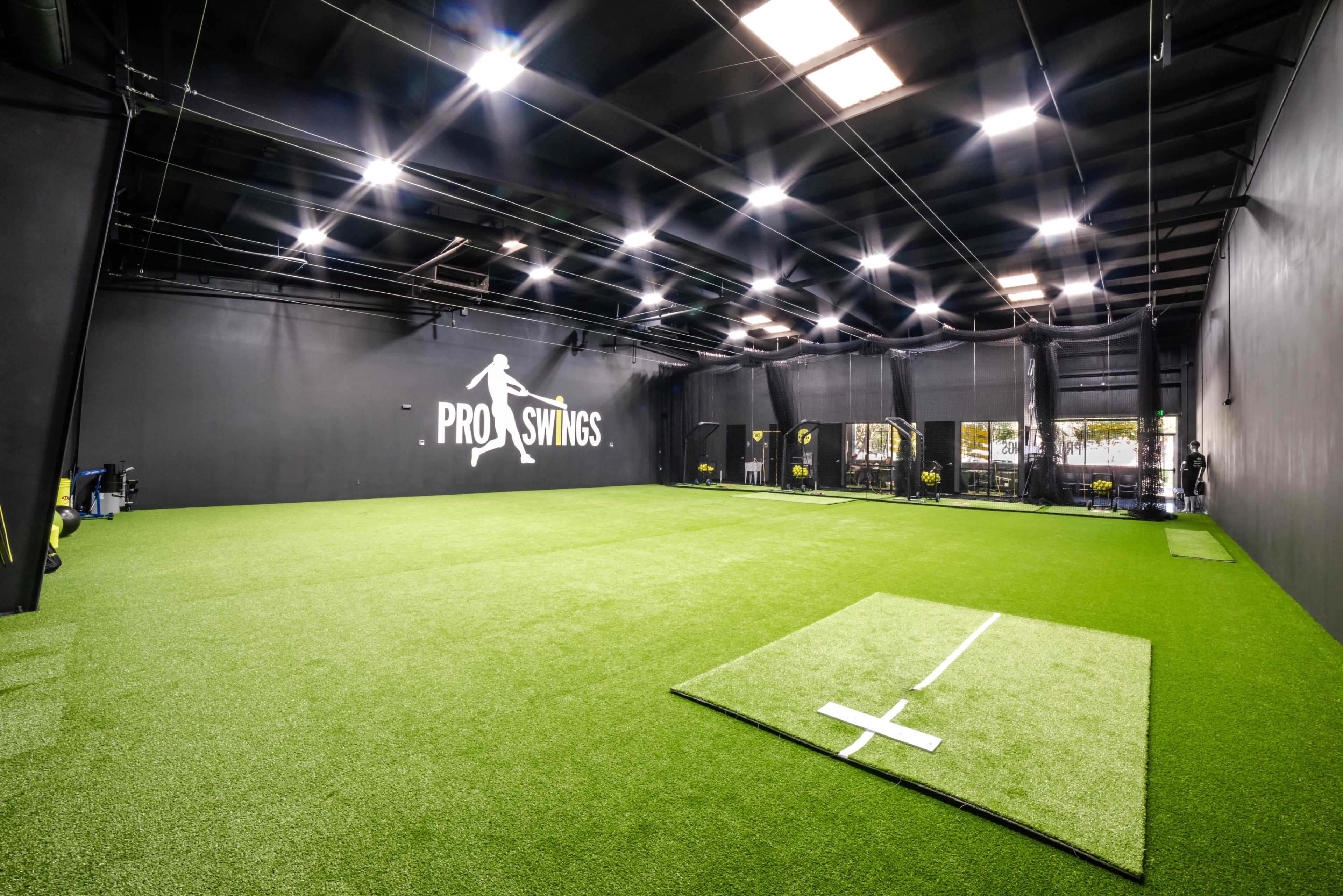 The image shows an indoor sports facility featuring artificial turf, batting cages, and a prominent wall sign with the text "PRO SWINGS."