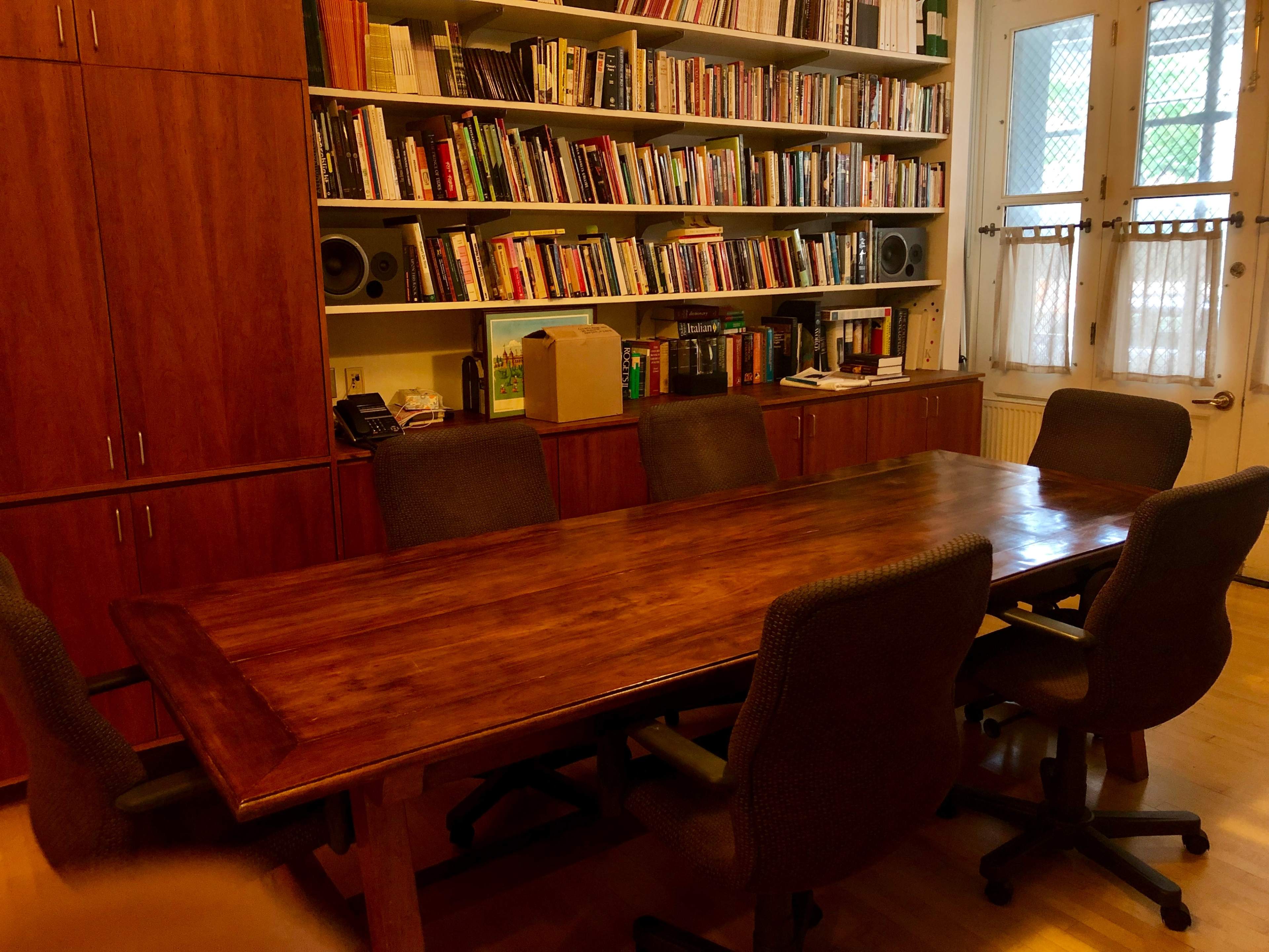 A wooden conference table is surrounded by five chairs in a room filled with bookshelves and cabinets.