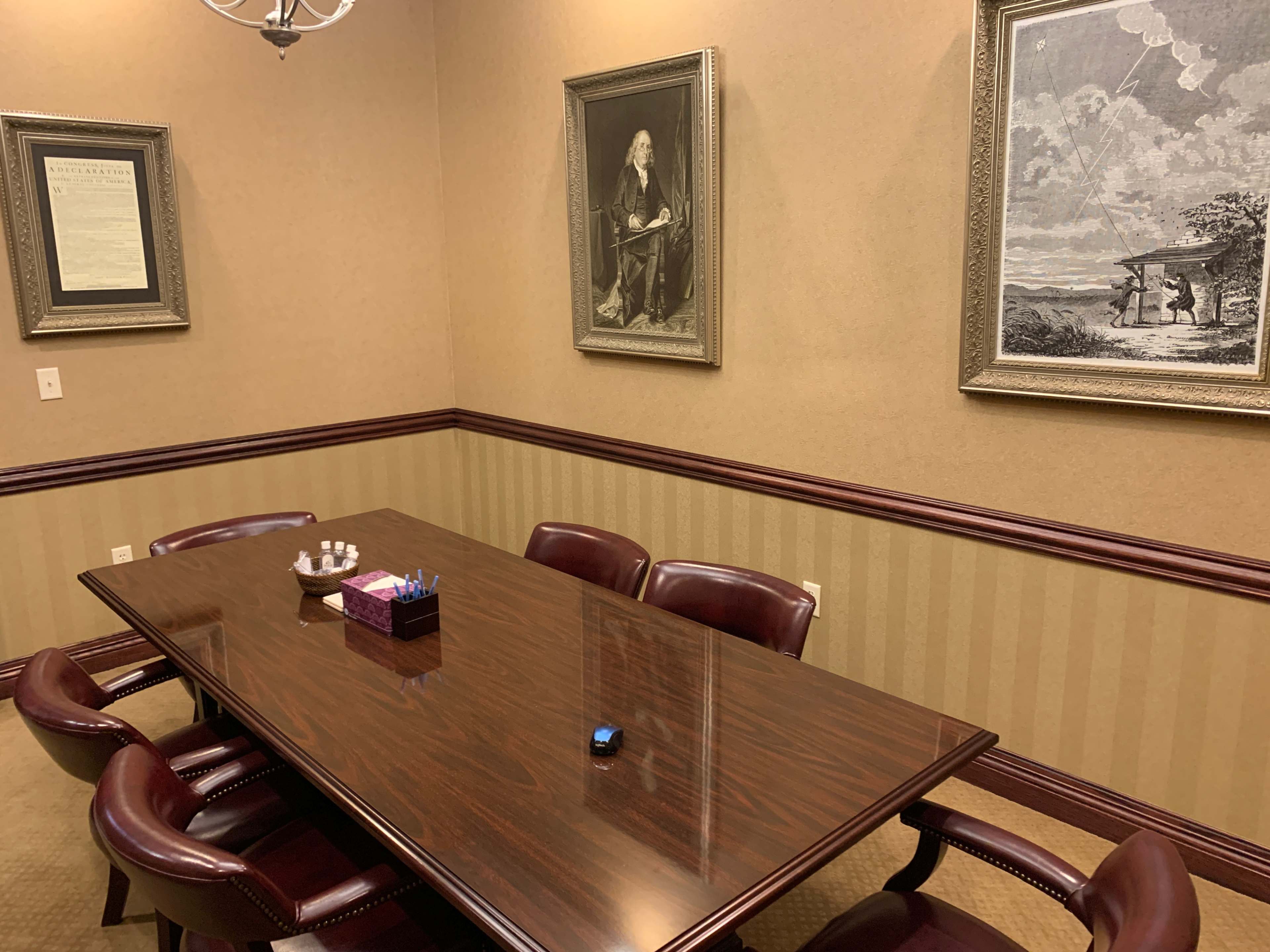 A conference room with a wooden table surrounded by leather chairs, featuring framed artwork on the walls and a decorative centerpiece on the table.
