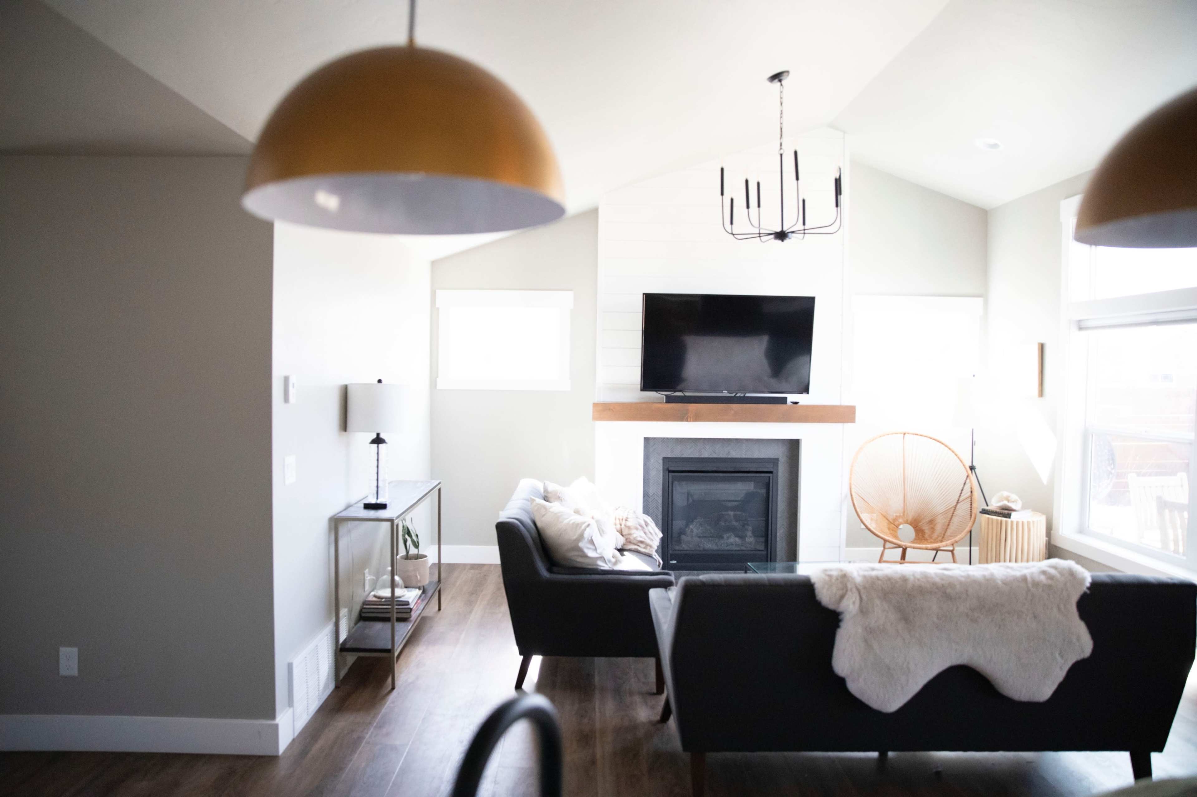 A modern living room featuring a fireplace, a flat-screen TV mounted above the mantel, stylish furniture, and large windows allowing natural light.