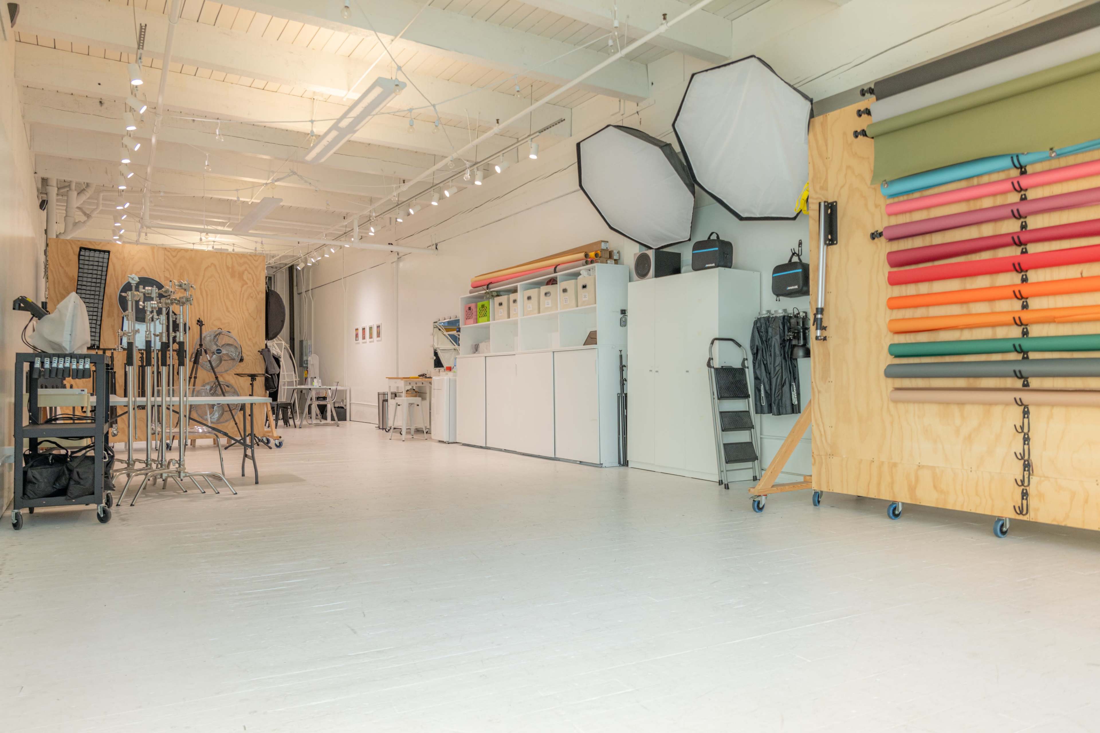A spacious photo studio with a variety of backdrops organized on the wall, lighting equipment, and storage cabinets neatly arranged.