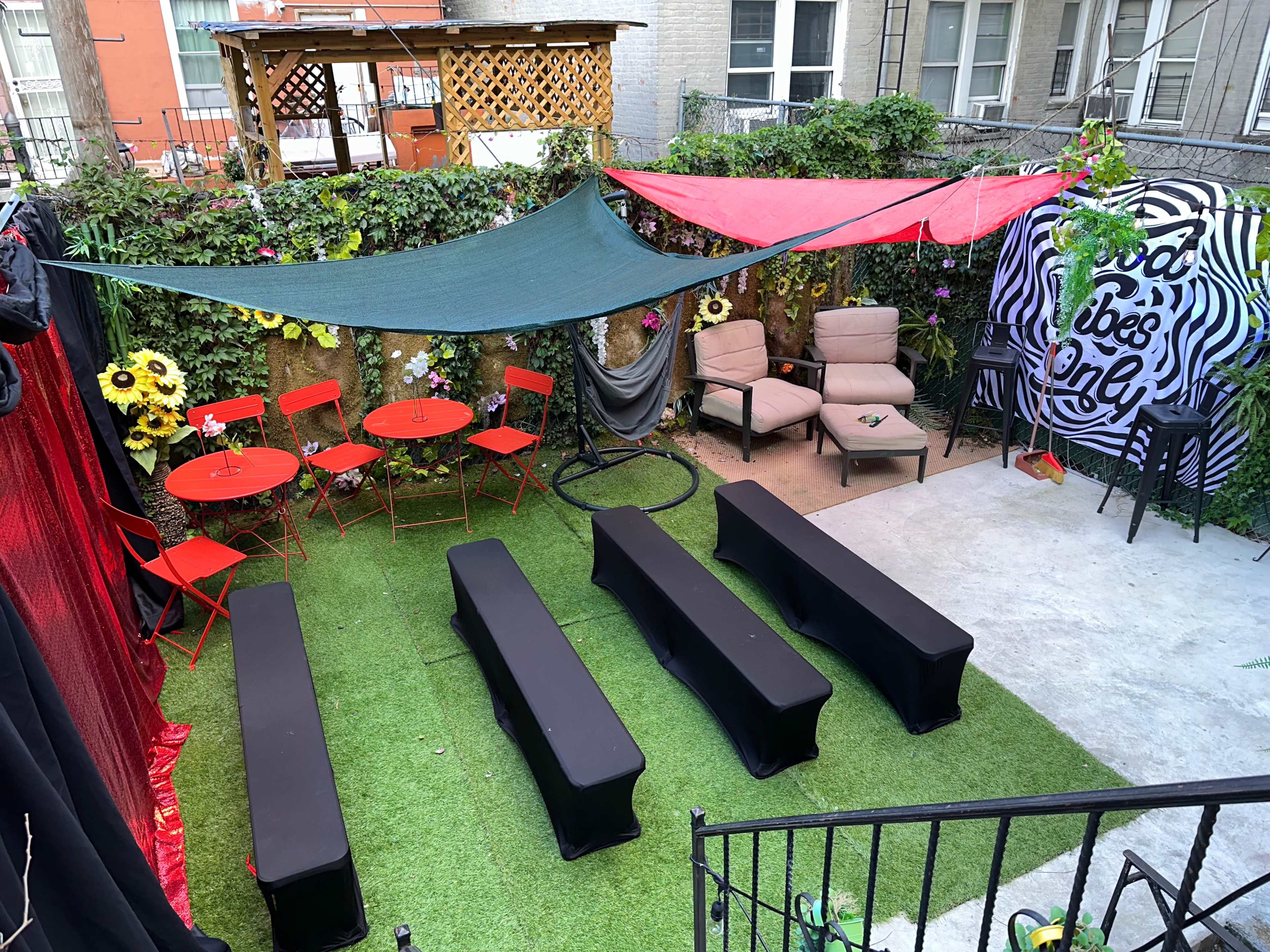A small outdoor venue with green grass, red and green canopies, seating areas, and decorated walls, ready for an event.